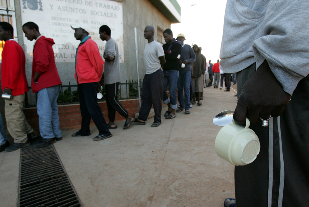 African migrants hold cups as they wait to have breakfast