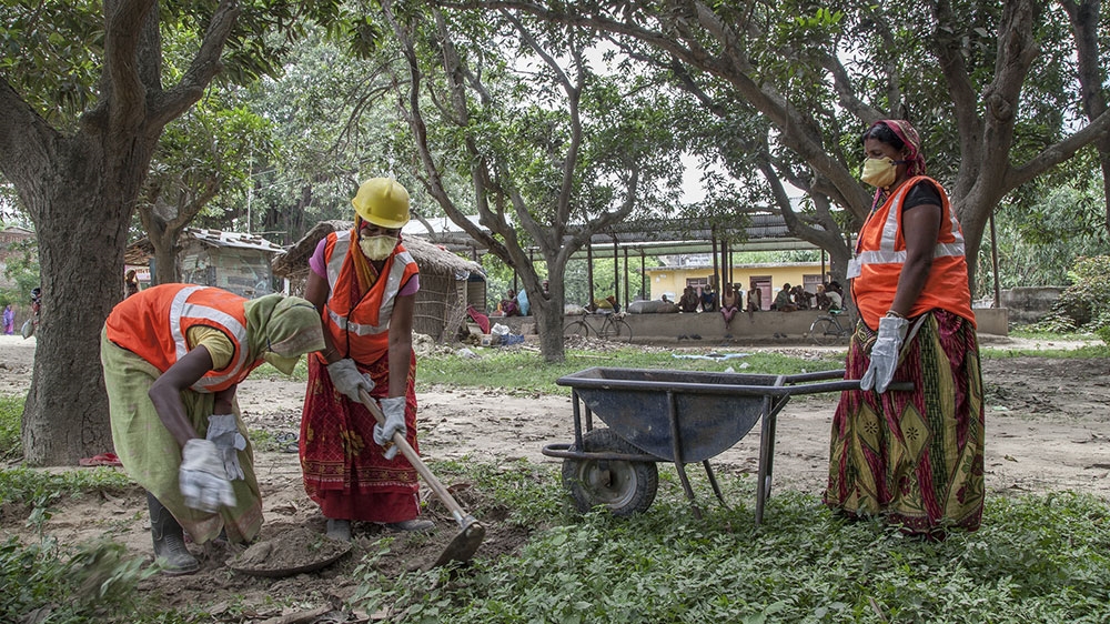 A group of Maithil women clear grass from the sides of a rural road where they work as road maintenance staff [Omar Havana/Al Jazeera]