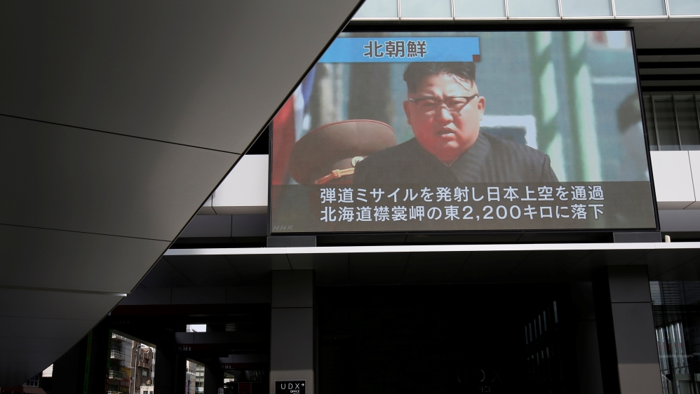 A passerby walks under a TV screen reporting news