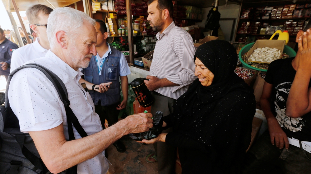 A Syrian refugee woman offers sweets to Corbyn during his visit to al-Zaatari refugee camp [Muhammad Hamed/Reuters]