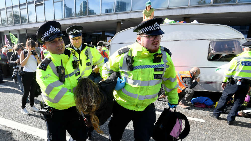 Police officers carry away an activist as Extinction Rebellion protesters block the road outside MI5 headquarters