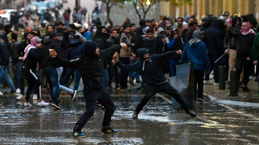 Anti-government protesters hurl stones at Lebanese riot police behind a barrier during a rally outside of the Lebanese Parliament in downtown Beirut, Lebanon, 22 January 2020. Lebanon announced on 21 