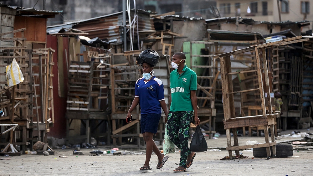 People wearing face masks walk past closed street stalls and shops due to a government ban on the operation of non-essential businesses and markets to halt the spread of the new coronavirus, in Lagos,