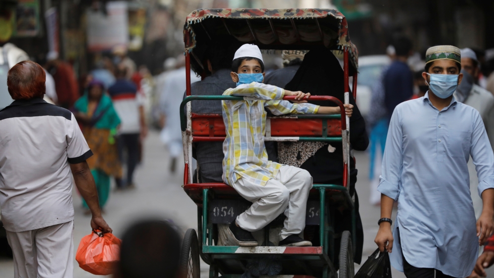 A boy wearing a protective face mask rides in a cycle rickshaw in Delhi, India