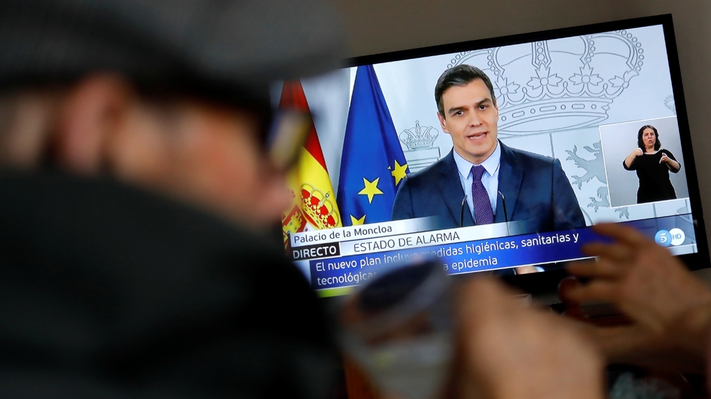 An elderly couple eats lunch at their home as they watch Spanish Prime Minister Pedro Sanchez on a television screen during a live news conference, due to the coronavirus disease (COVID-19) outbreak, 