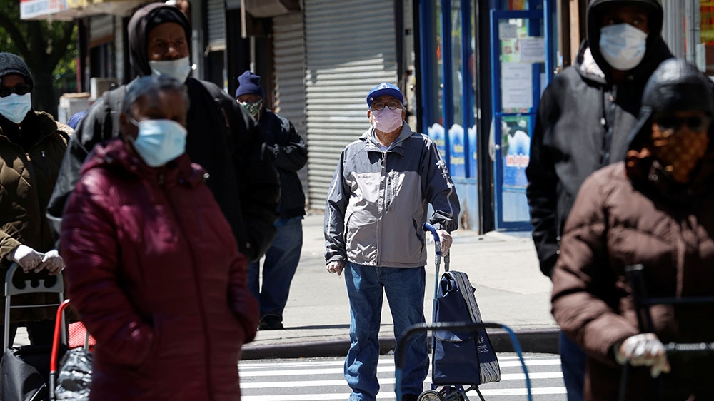 People wearing protective face masks wait in line at a free food distribution for people in need, outside the West Harlem Group Assistance in Manhattan