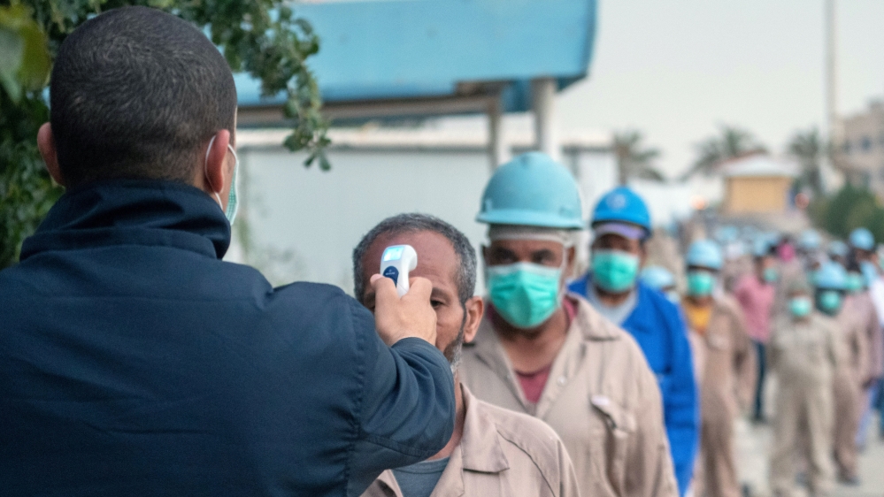 A security employee checks temperatures of labourers before entering a construction worksite, following the outbreak of COVID-19, in Ahmadi, Kuwait