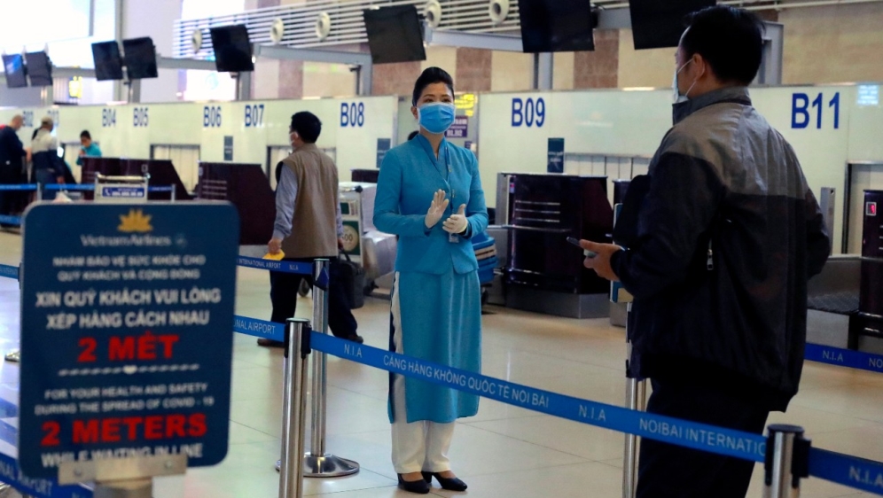 An airline staff member instructs passengers how to check in at Hanoi airport while observing social distancing