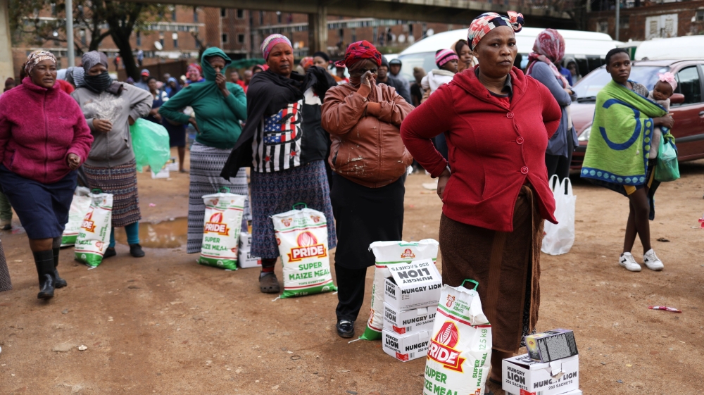 Locals look on during the distribution of food amid the spread of the coronavirus in Alexandra township, South Africa