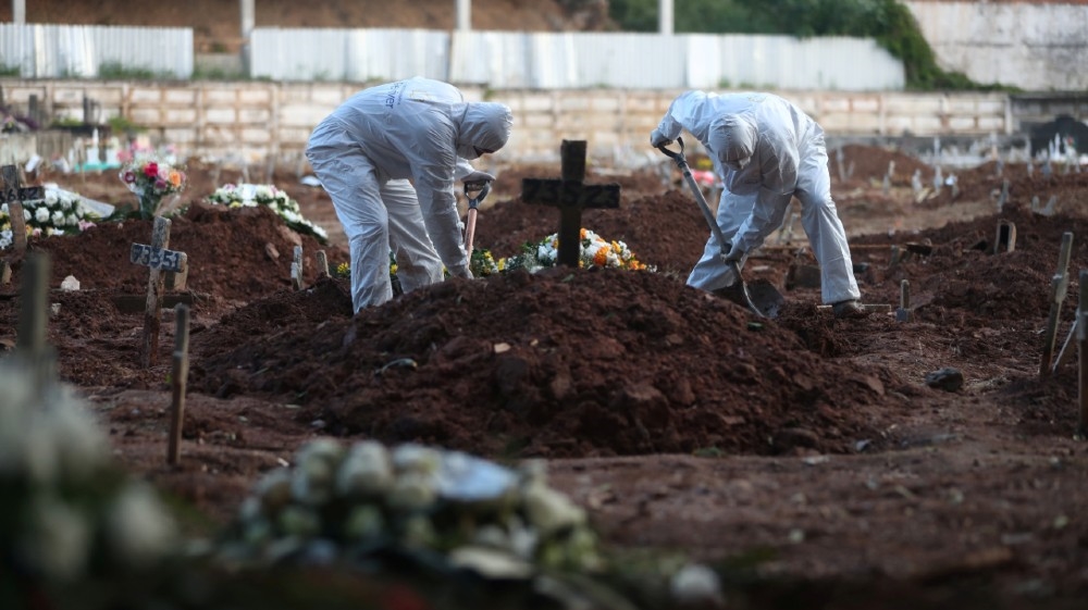 Gravediggers wearing protective garments work as relatives of a victim who died of the coronavirus disease (COVID-19), attend her burial at a cemetery in Rio de Janeiro, Brazil