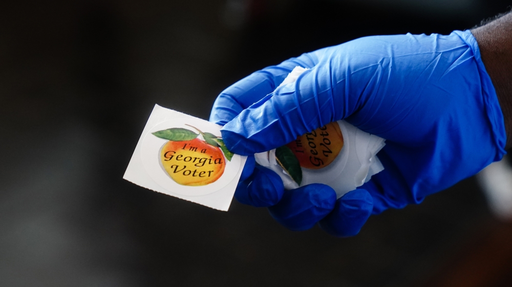 A polling place worker holds an "I''m a Georgia Voter" sticker to hand to a voter on June 9, 2020 in Atlanta, Georgia. Georgia, West Virginia, South Carolina, North Dakota, and Nevada are holding prim