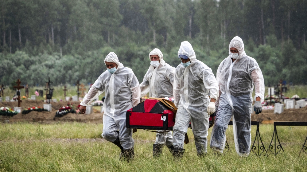Cemetery workers wearing protective suits carry the coffin of a COVID-19 victim in the special purpose for coronavirus victims section of a cemetery in Kolpino, outside St.Petersburg, Russia, Tuesday,