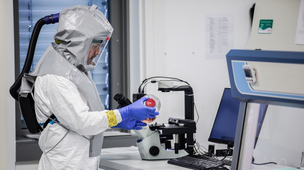 A lab technician wearing a full body protection suit handles a bottle containing growth media for virus production during coronavirus vaccine research at the Valneva SA laboratories in Vienna, Austria