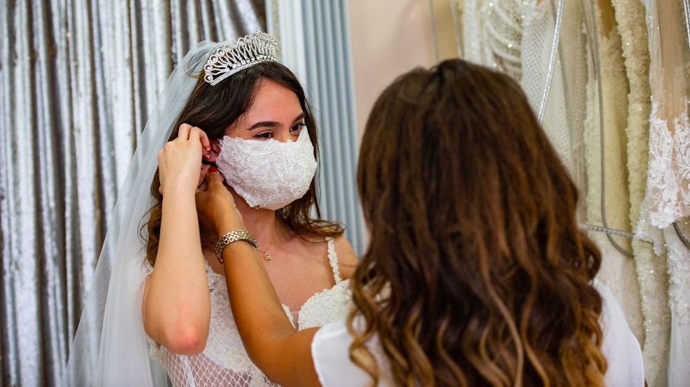 TURKEY-HEALTH-VIRUS-WEDDING-FASHION Wedding Dress designer Pinar Bent (back) adjusts a mannequin wearing a wedding dress with matching protective mask in her store in Istanbul, on June 30, 2020.