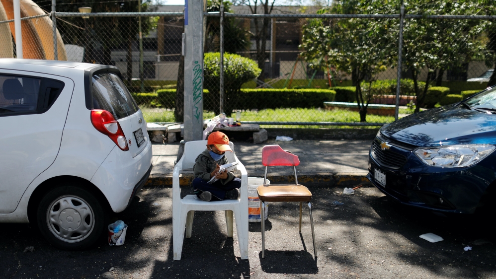 A boy does his homework along a street while waiting for his mother who works by receiving tips for looking after parked cars in Mexico City