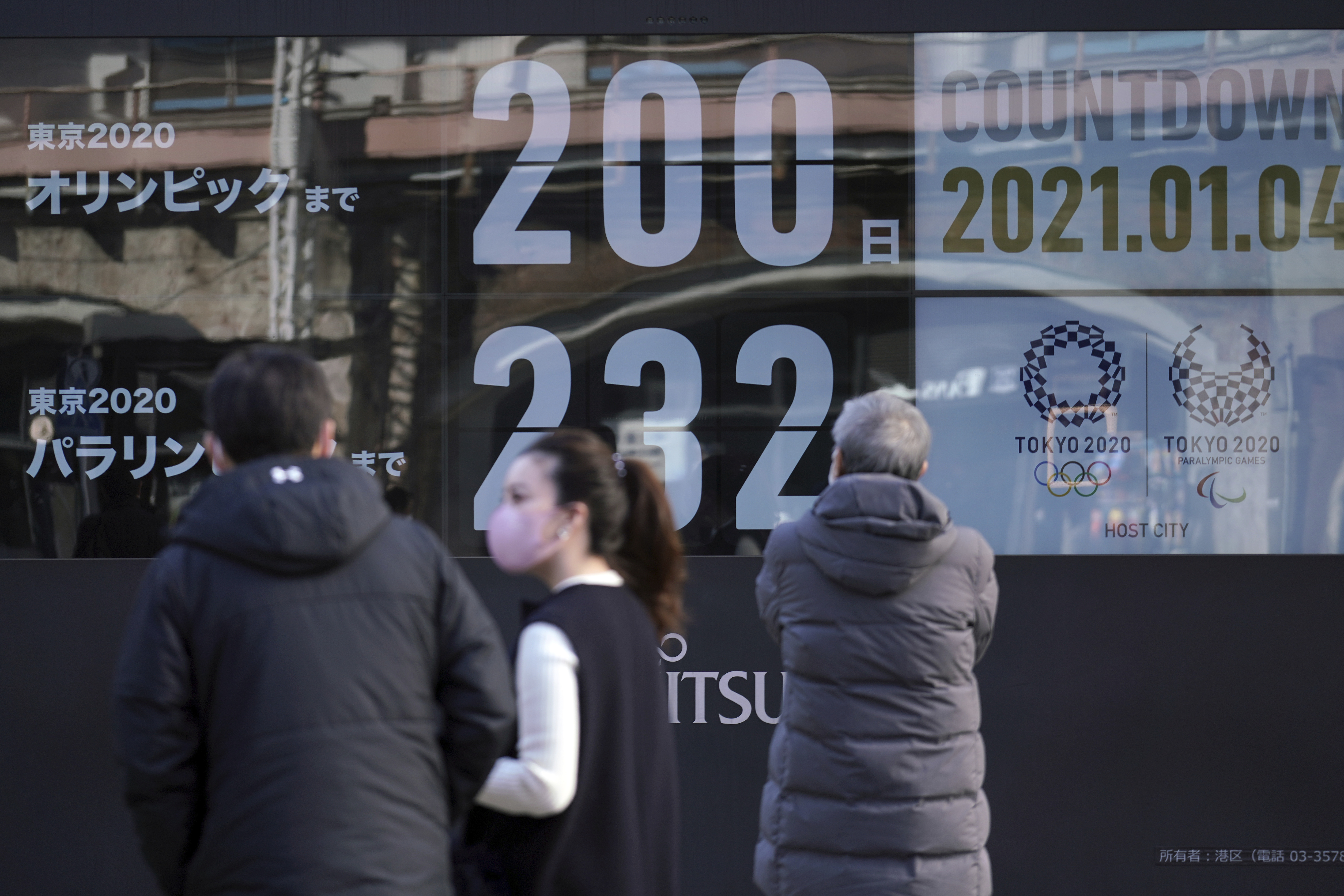 People wearing masks against the spread of the coronavirus walk in front of a countdown calendar showing 200 days to the start of the Tokyo 2020 Olympics on Monday, January 4, 2021, in Tokyo