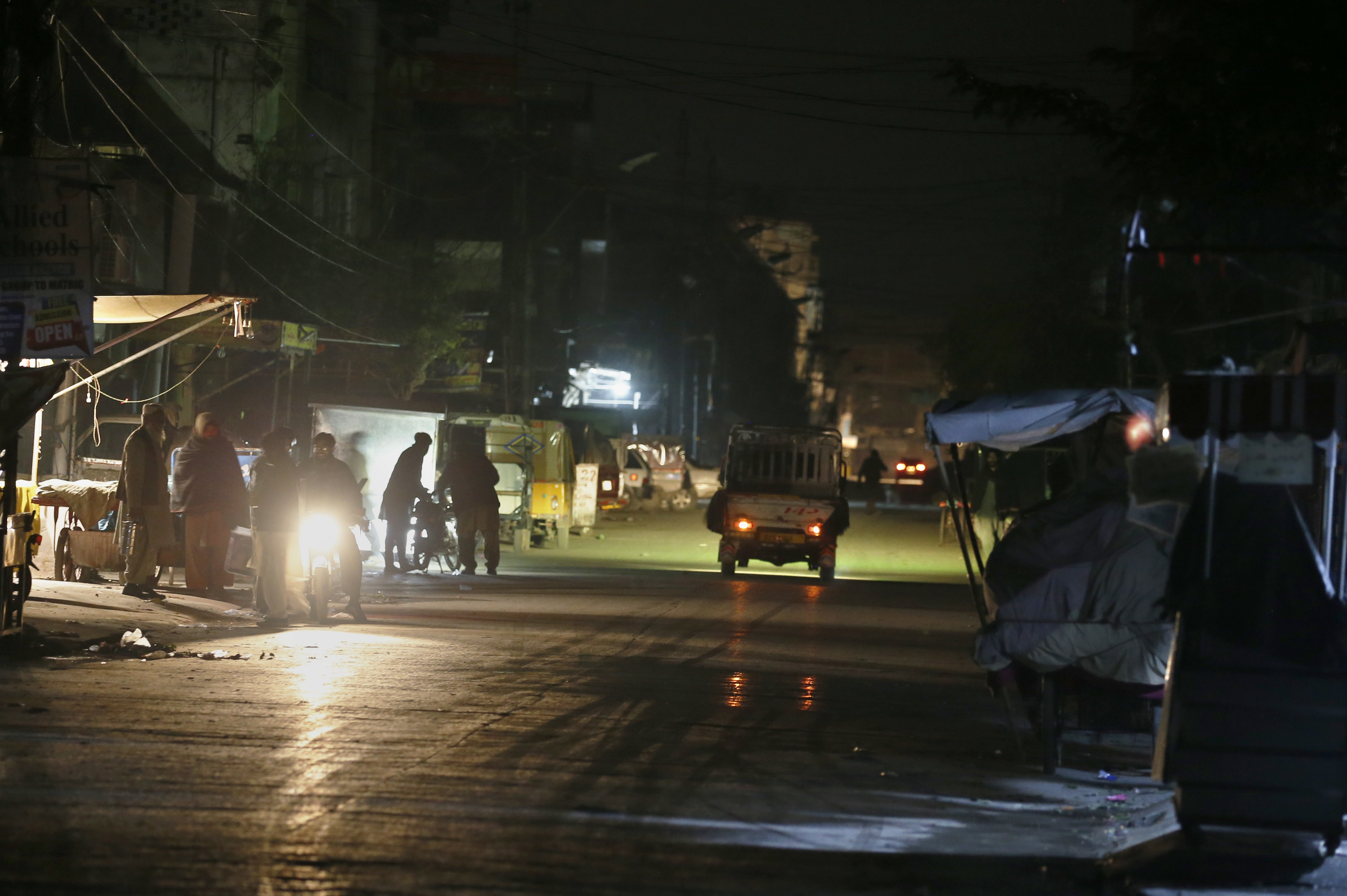 People are silhouetted on a vehicle’s headlights on a dark street during widespread power outages in Rawalpindi