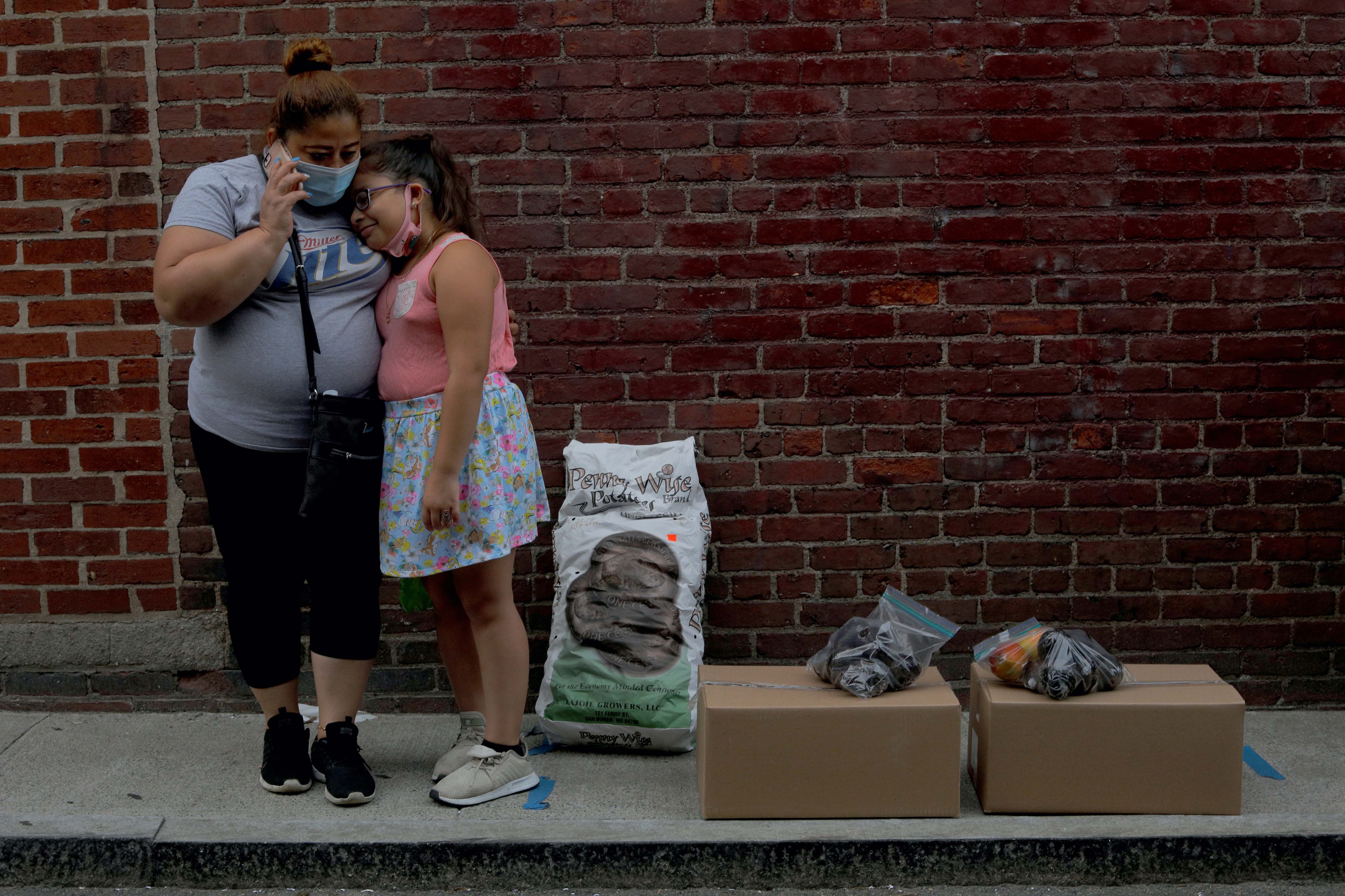 Sandra Cruz, who lost her job because of the coronavirus outbreak – and who fell four months behind on her rent and is fearing eviction – waits for a ride with her daughter Gabriella after picking up free groceries distributed by the Chelsea Collaborative in Chelsea, Massachusetts, the US