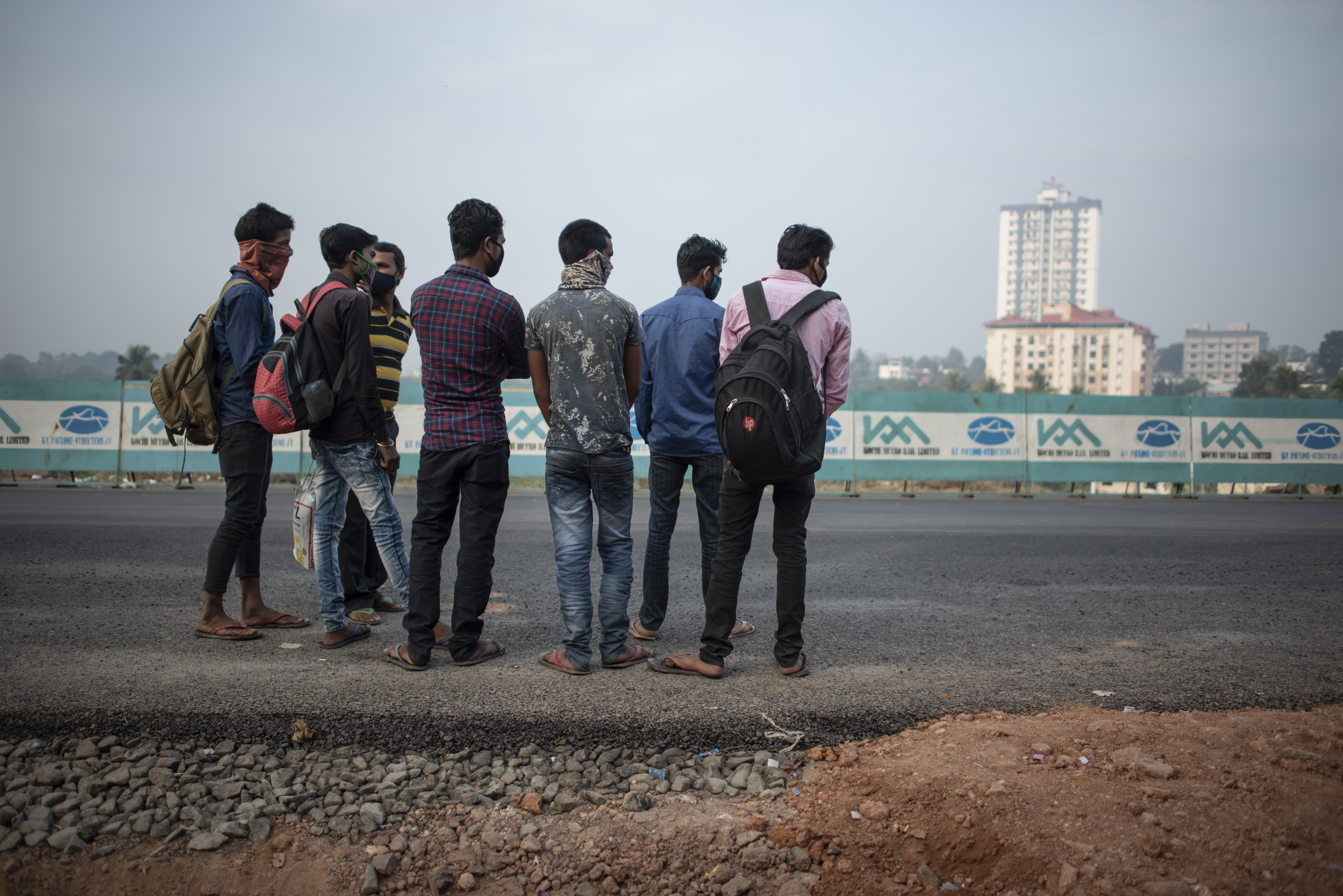 Migrant workers wearing face masks wait for transport in Kochi