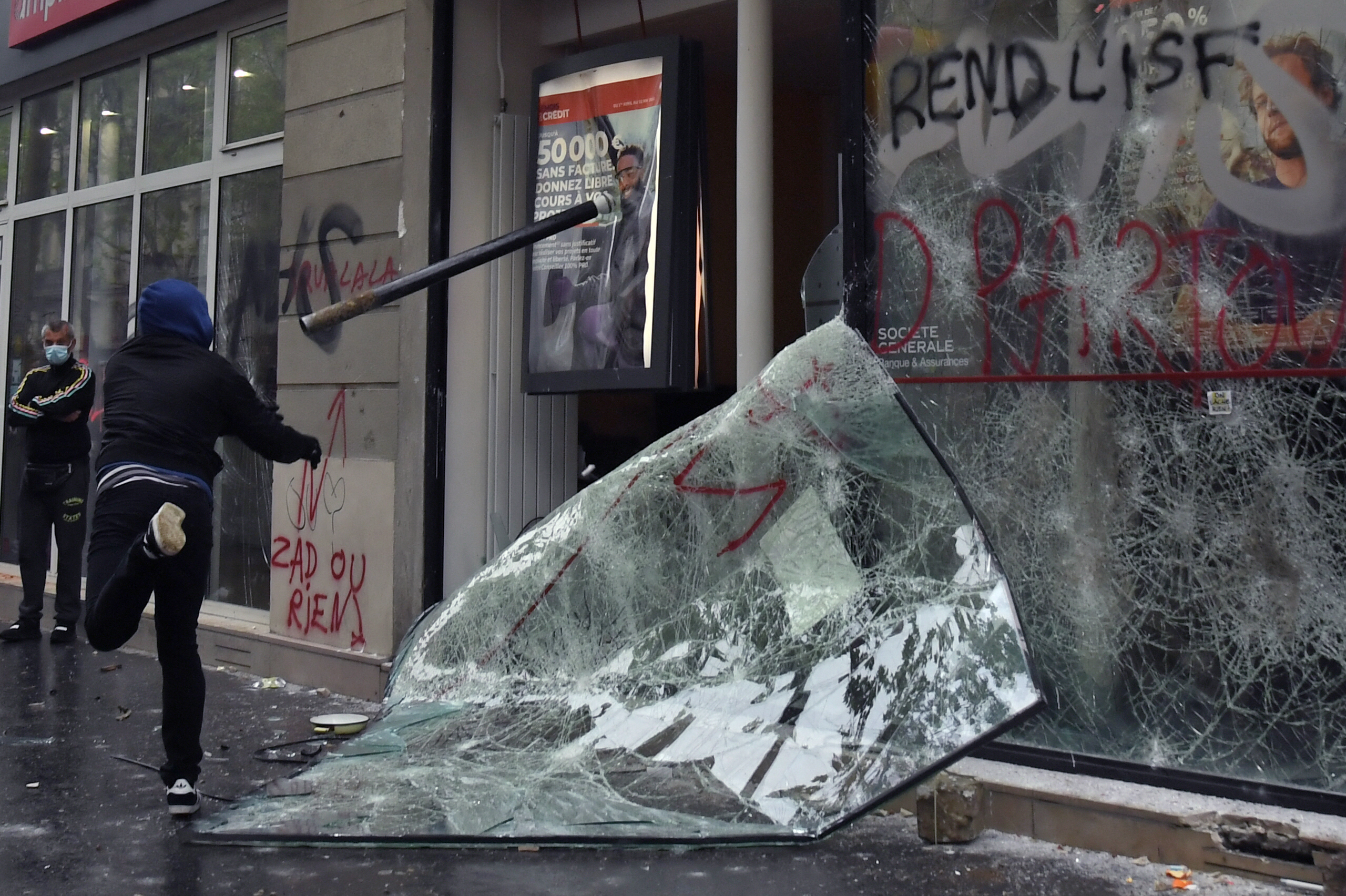 A protester throws a pole at a damaged bank in Paris