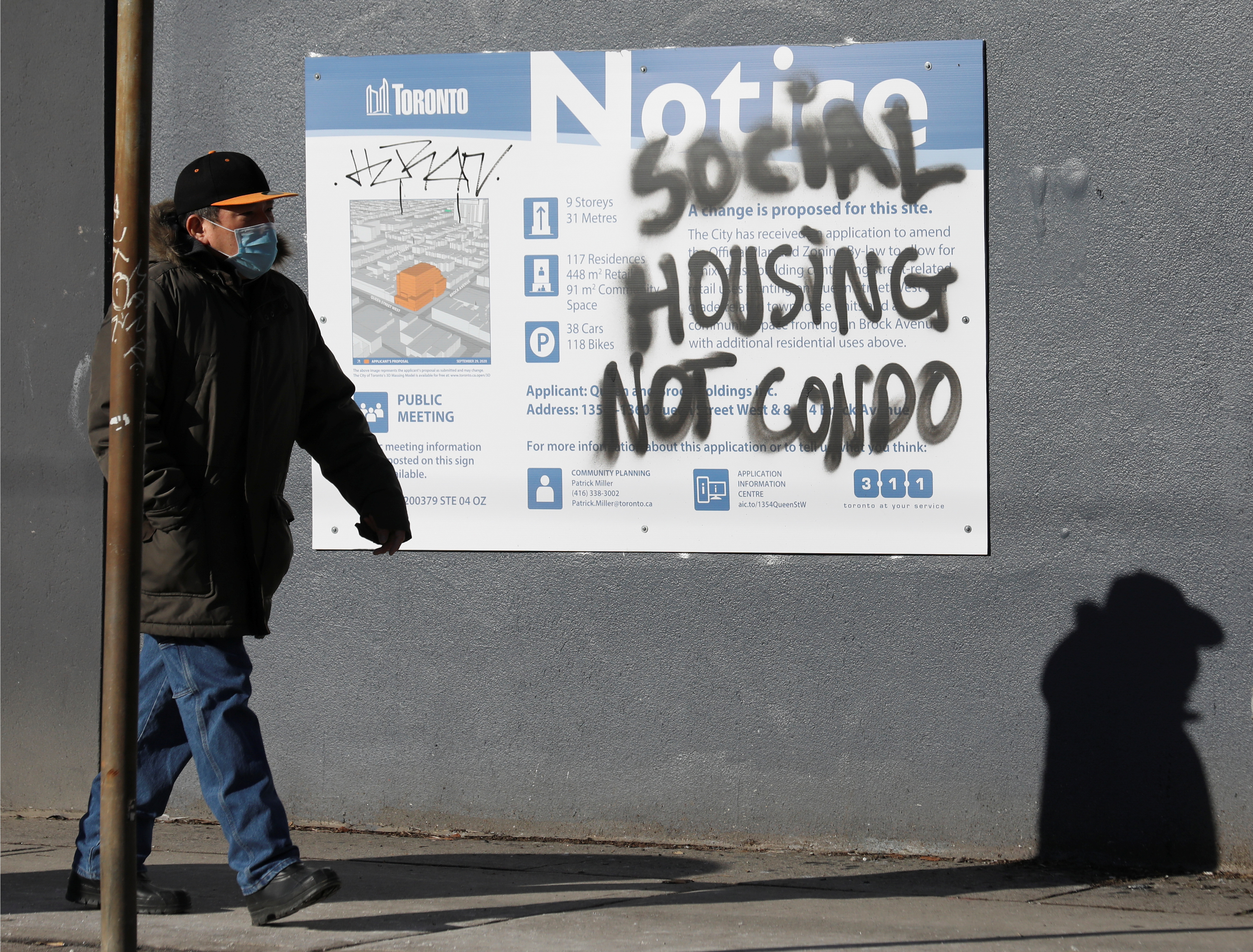 A person passes graffiti covering the announcement of a condominium development in the Parkdale neighborhood of Toronto, Ontario, Canada