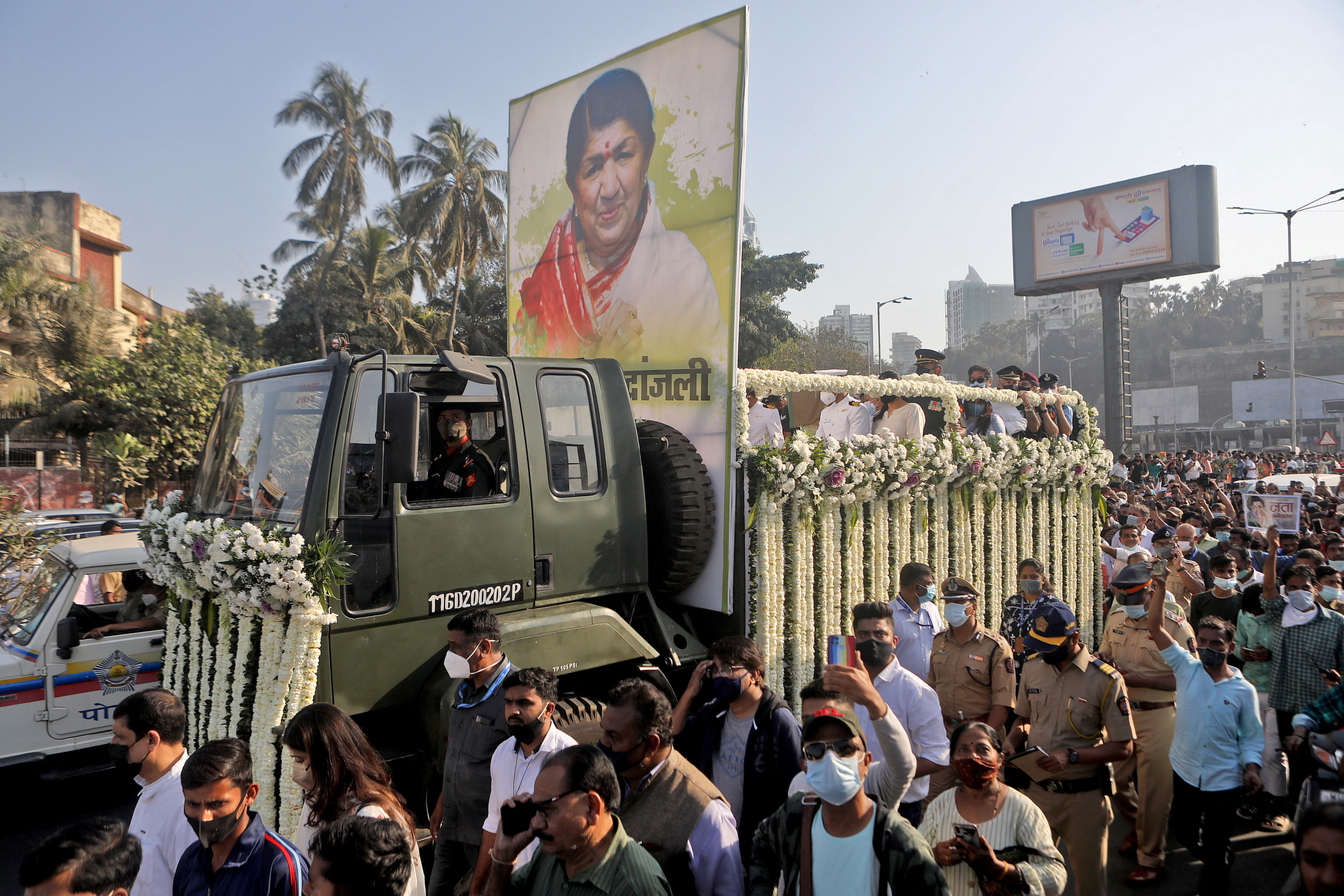 A military vehicle carrying the body of late Indian singer Lata Mangeshkar moves through a road crowded with people.