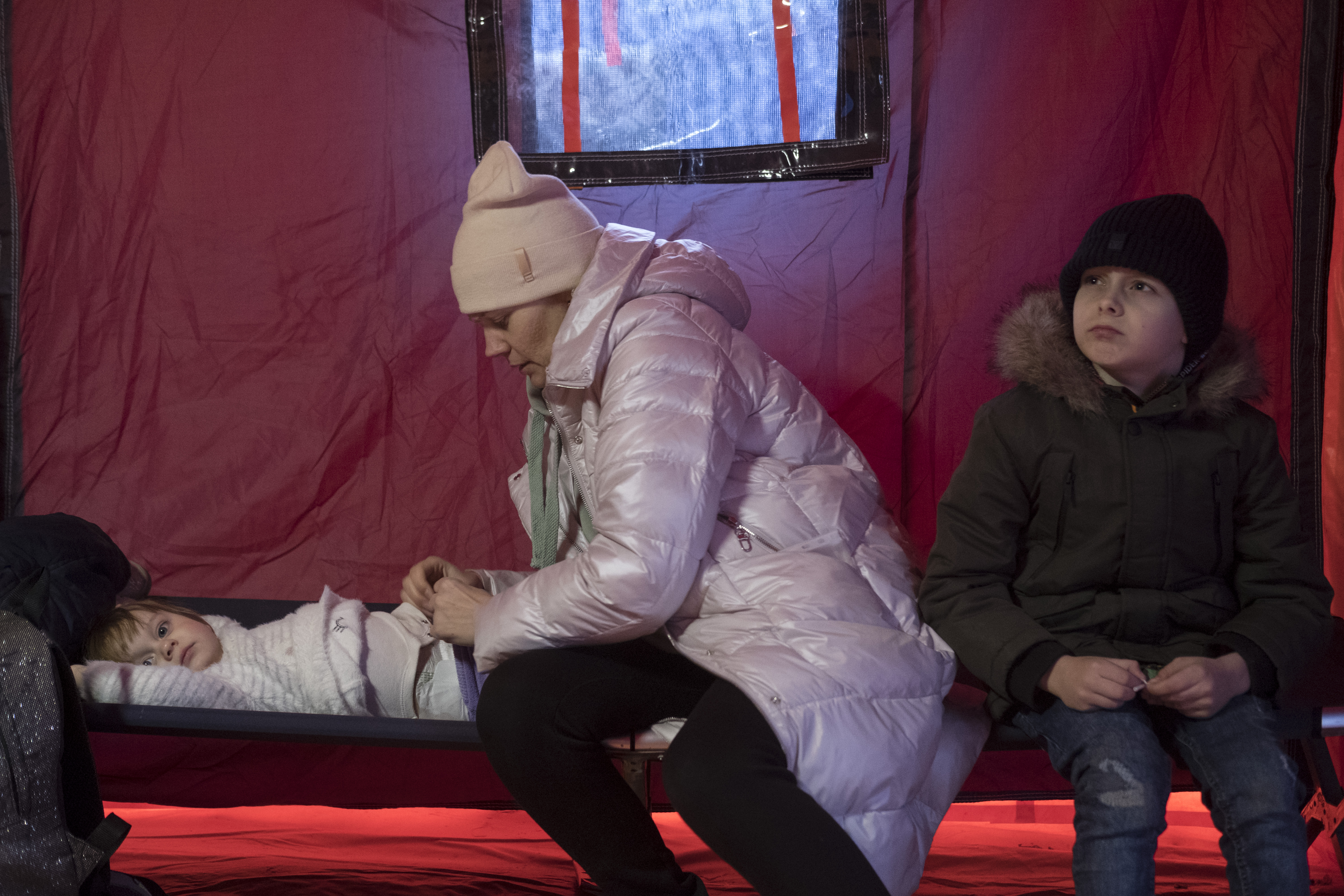 A Ukrainian mother tends to her children after the long journey in a temporary shelter tent nearby the Siret border crossing.