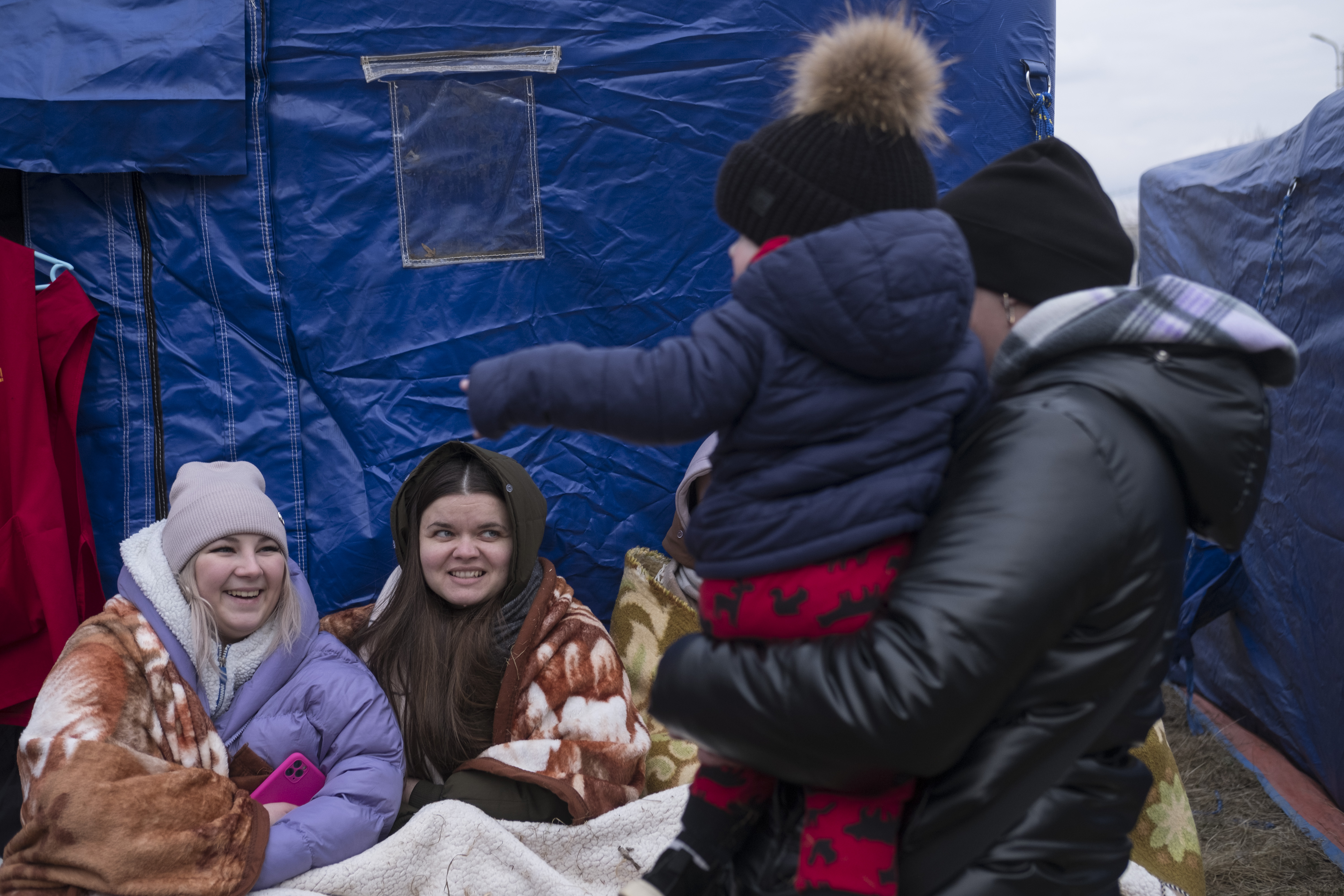 Women chat wrapped in blankets while waiting for transportation from the Siret border crossing to other towns in Romania.