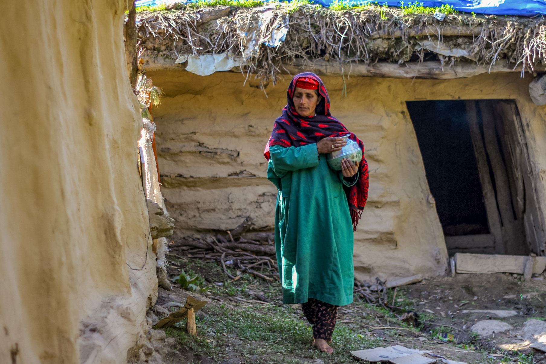 Zukaiha walking among the mud huts with a milk pot in her arms.