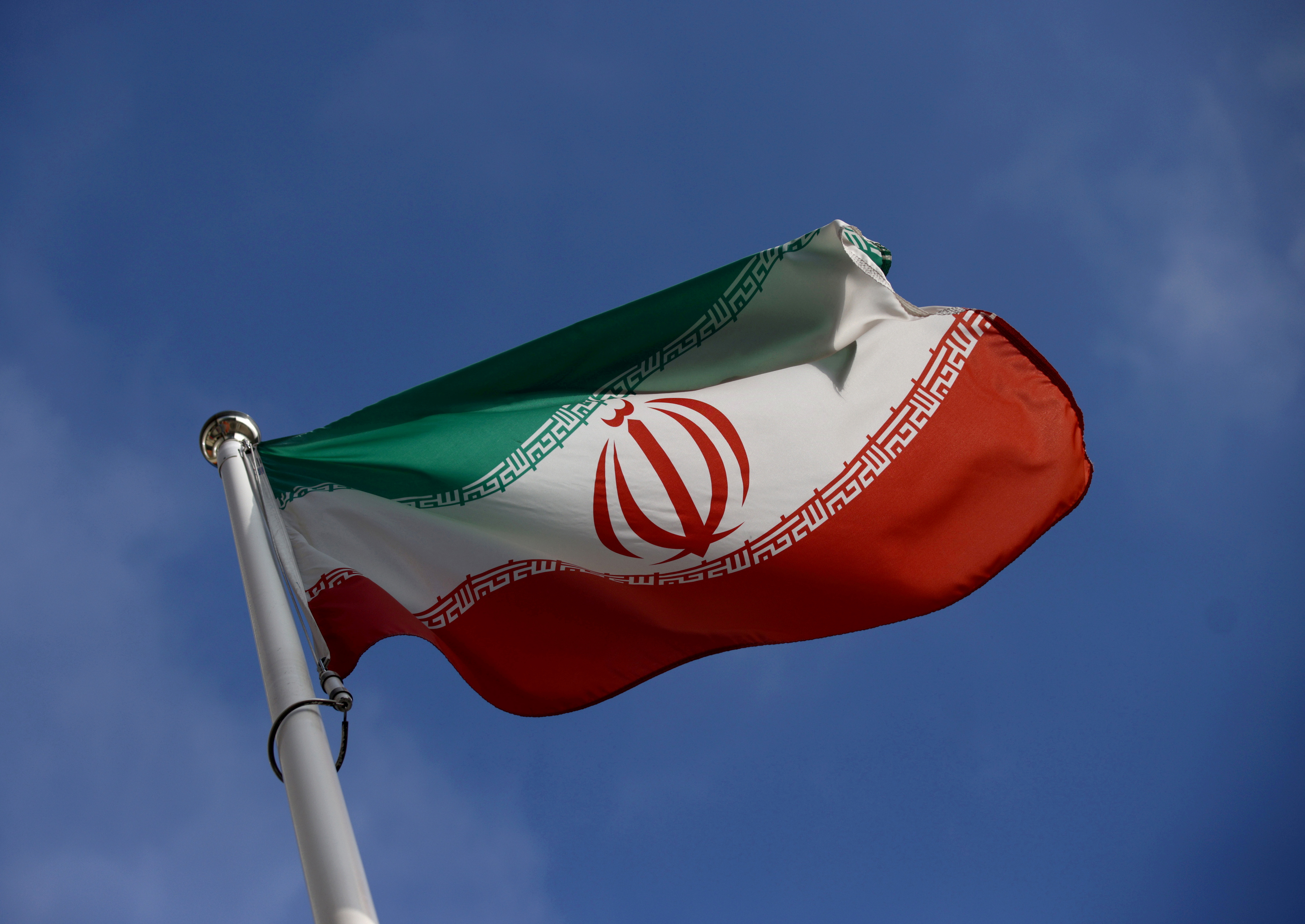 The Iranian flag flying on a pole against a blue sky.