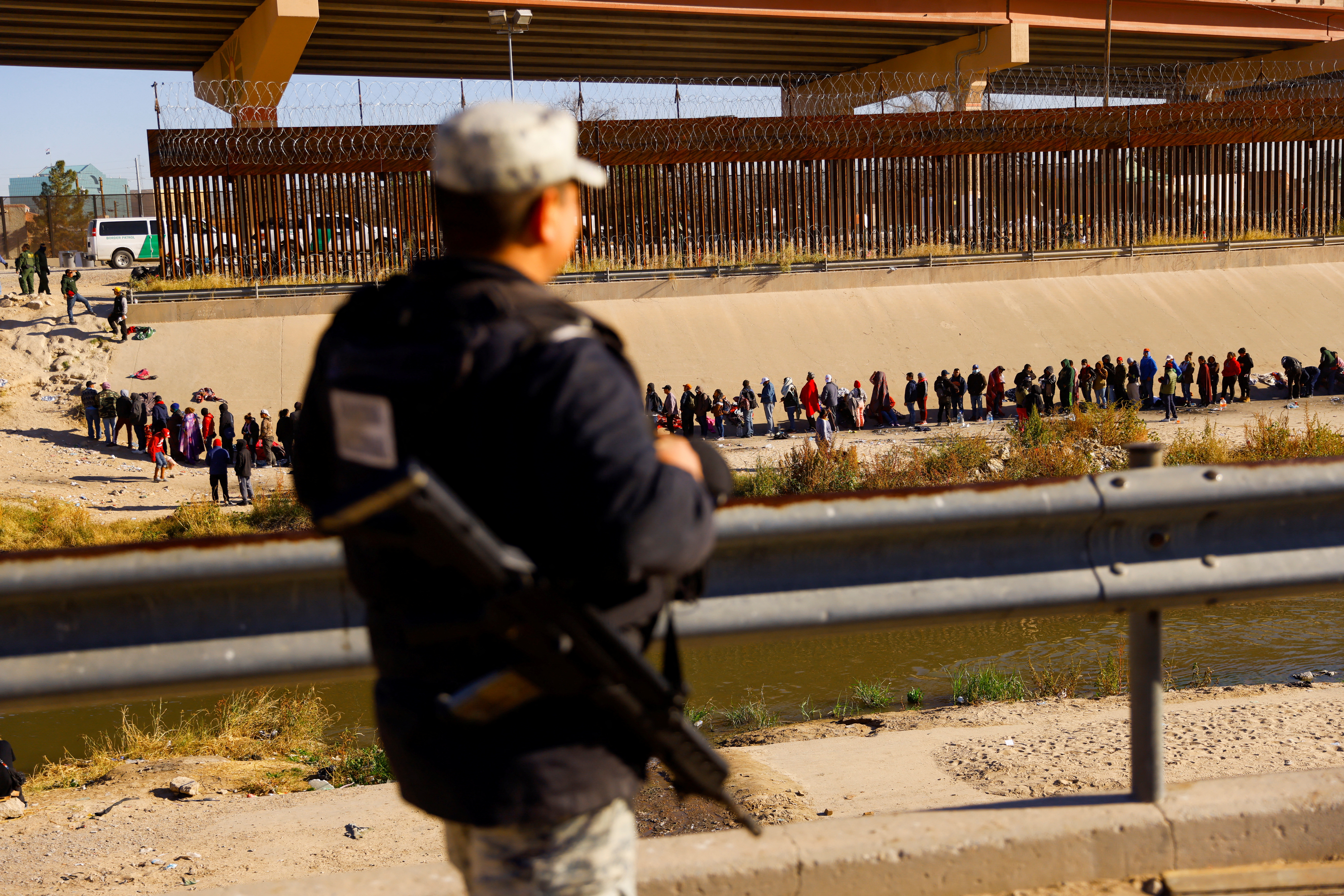 A soldier watches a line of people across the Rio Grande River.