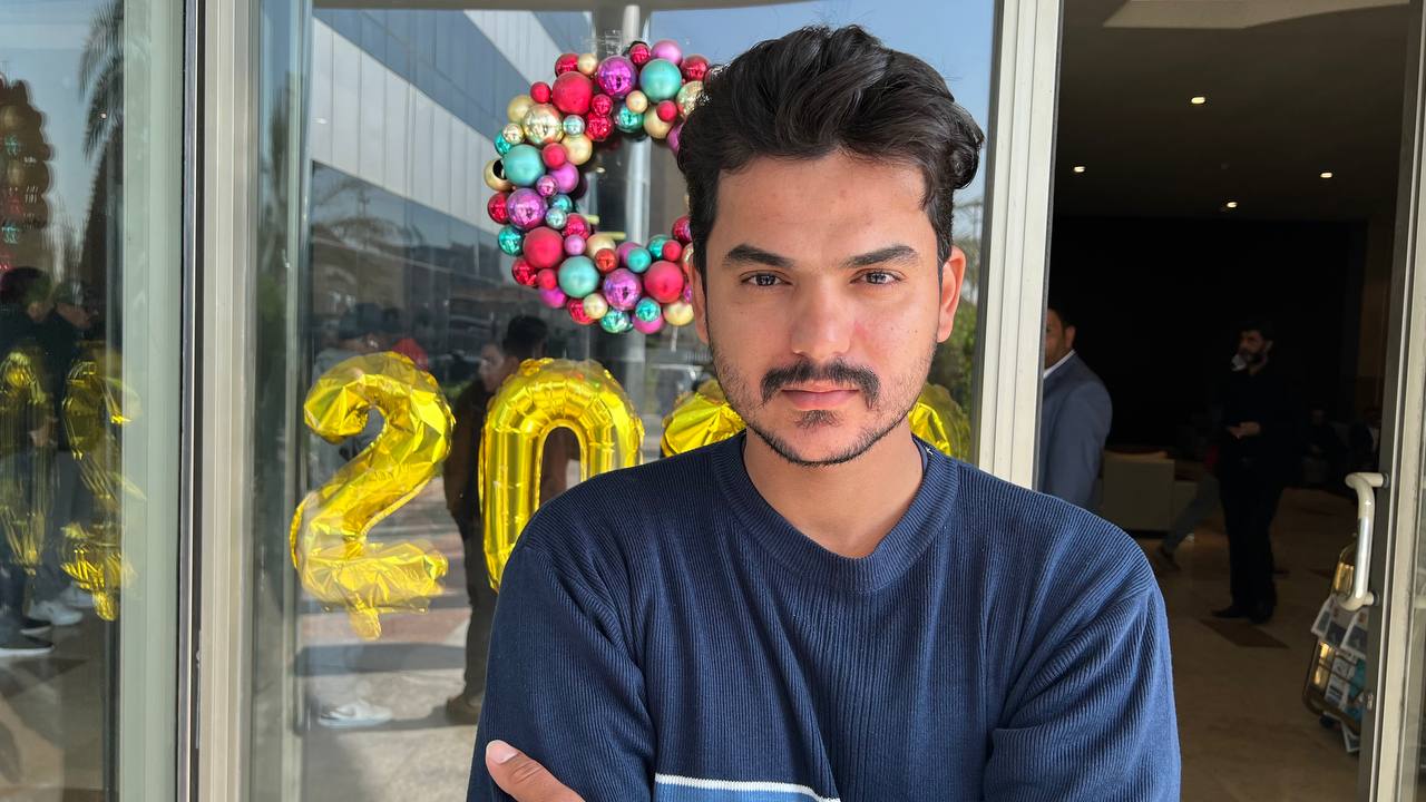 Ahmed Mustafa, a young man, stands in front of a glass door