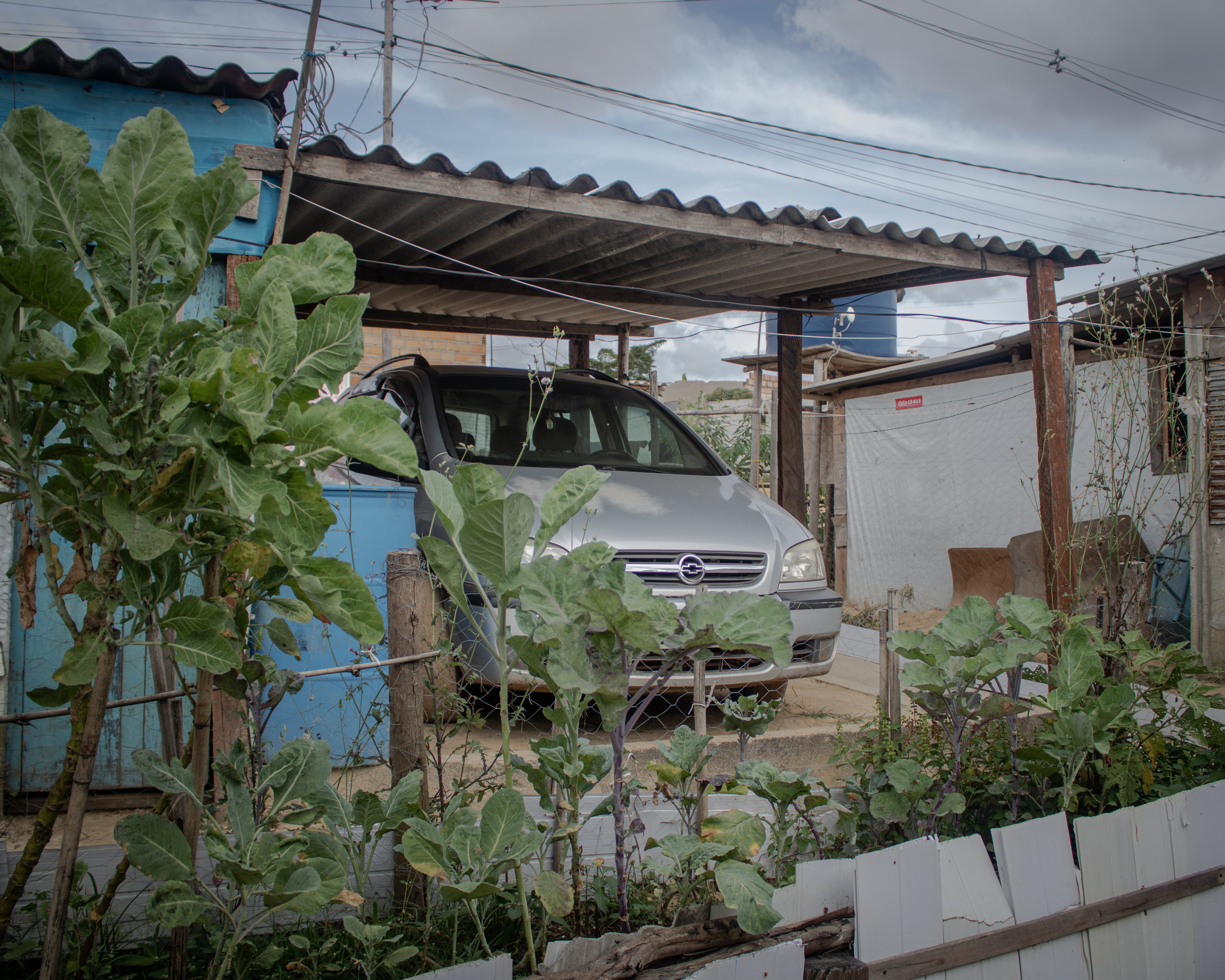 A photo of a car outside of a house, under a metal roof shade.