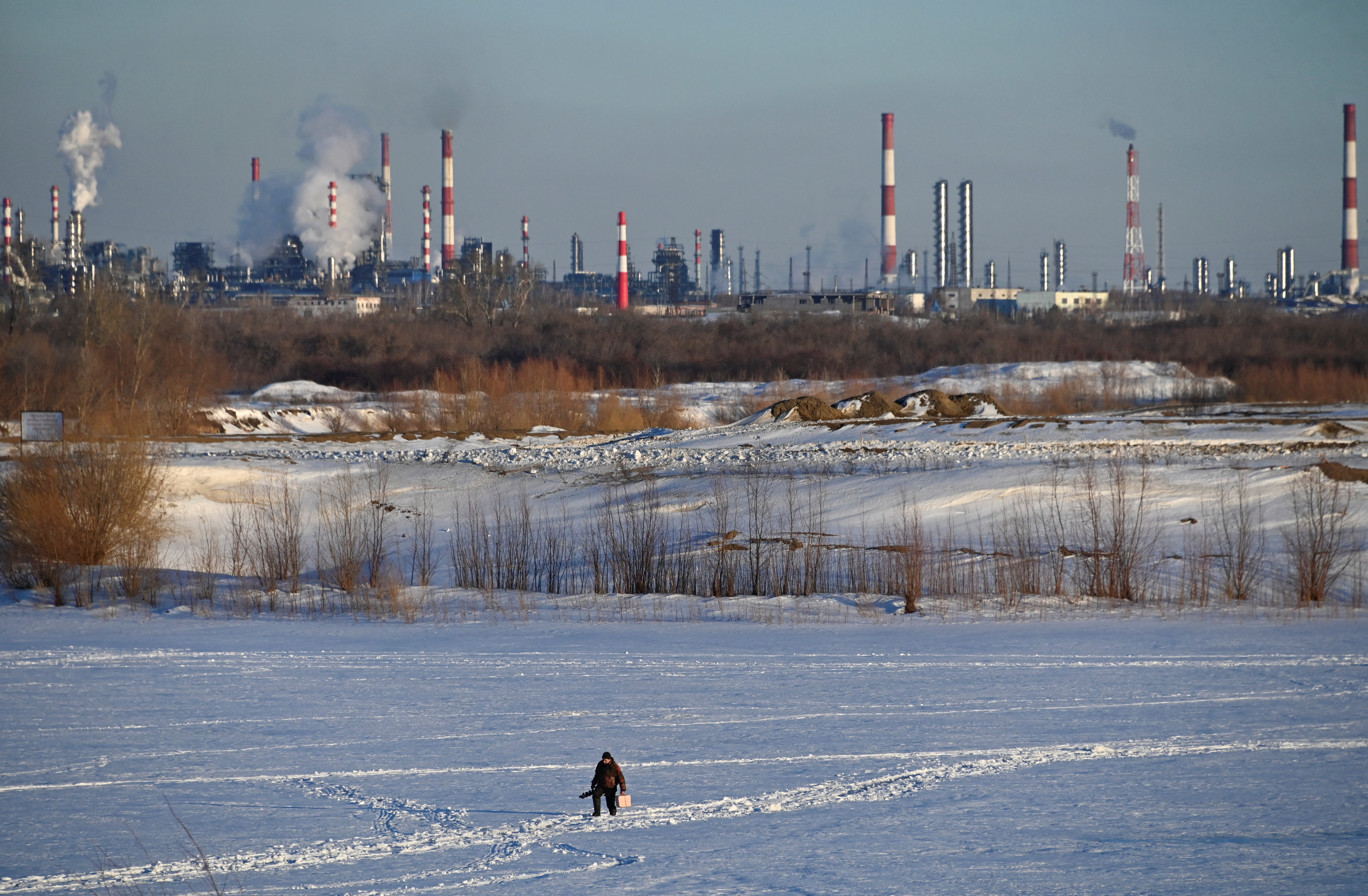 A fisherman walks on the ice-covered Irtysh River near an oil refinery and a thermal power station in the Siberian city of Omsk