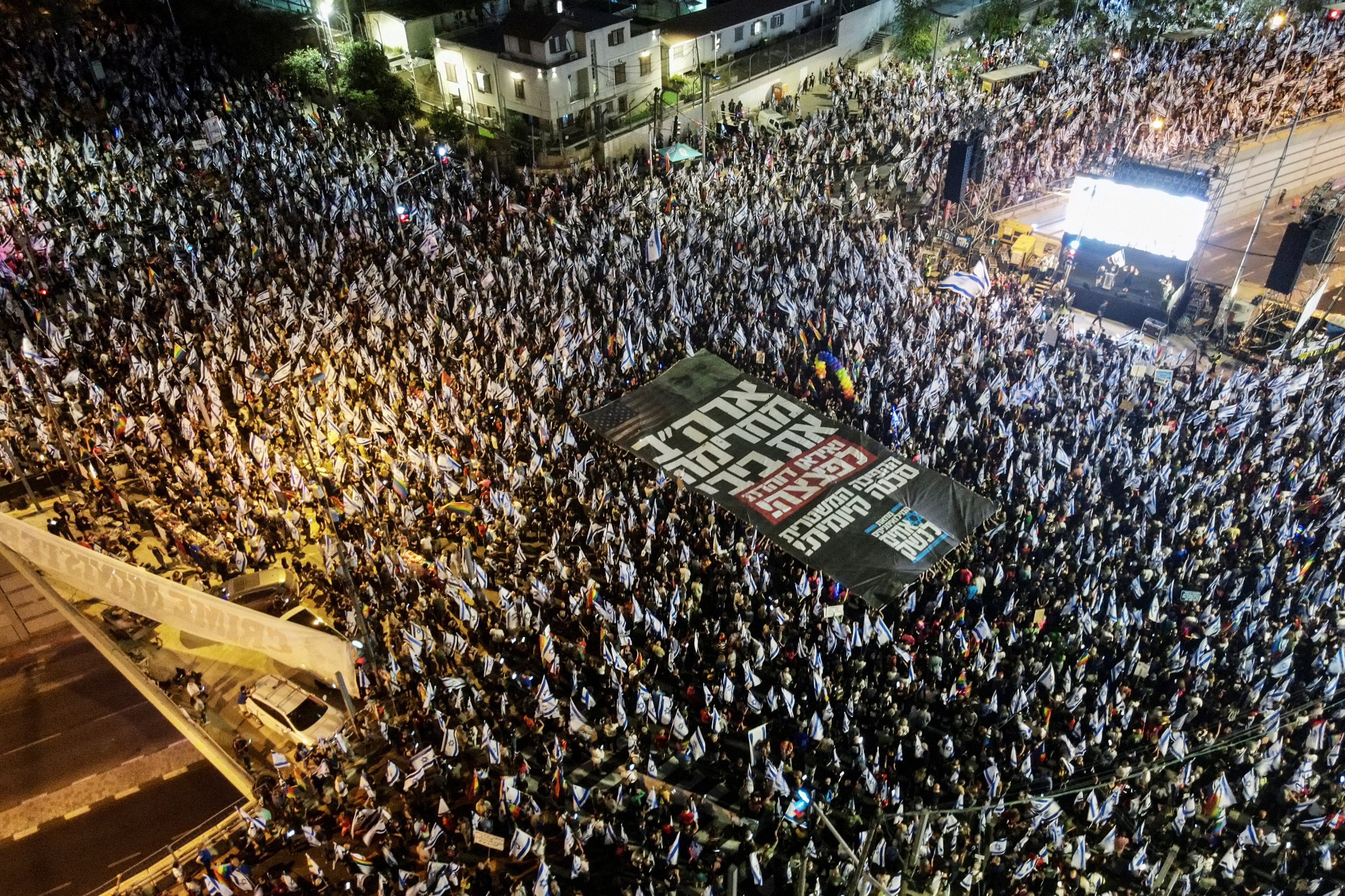 An aerial view shows protesters holding a banner with the Hebrew words "the U.S. is boycotting Bibi and Iran is galloping towards a bomb! The judicial overhaul is an existential threat!"