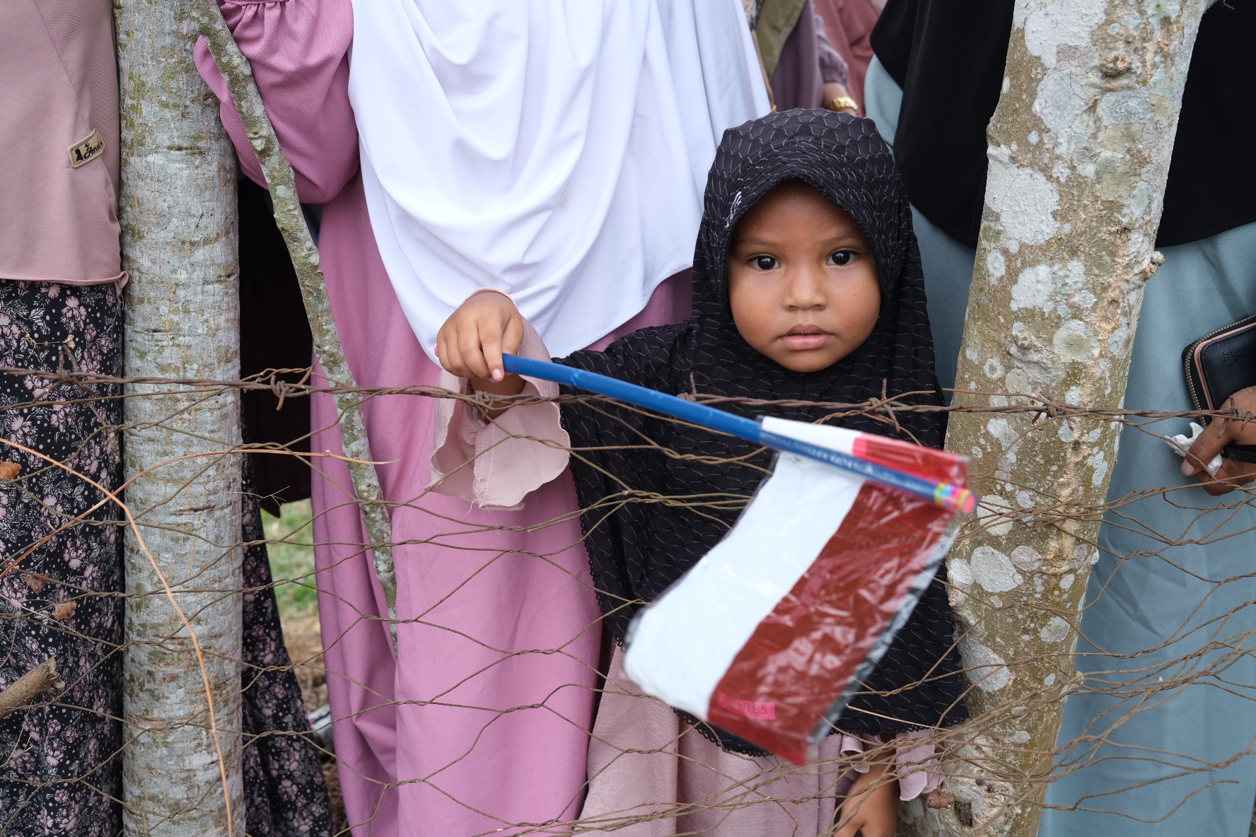 A young girl waits to see Indonesian President Joko Widodo. She is wearing a black headscarf and waving an Indonesian flag