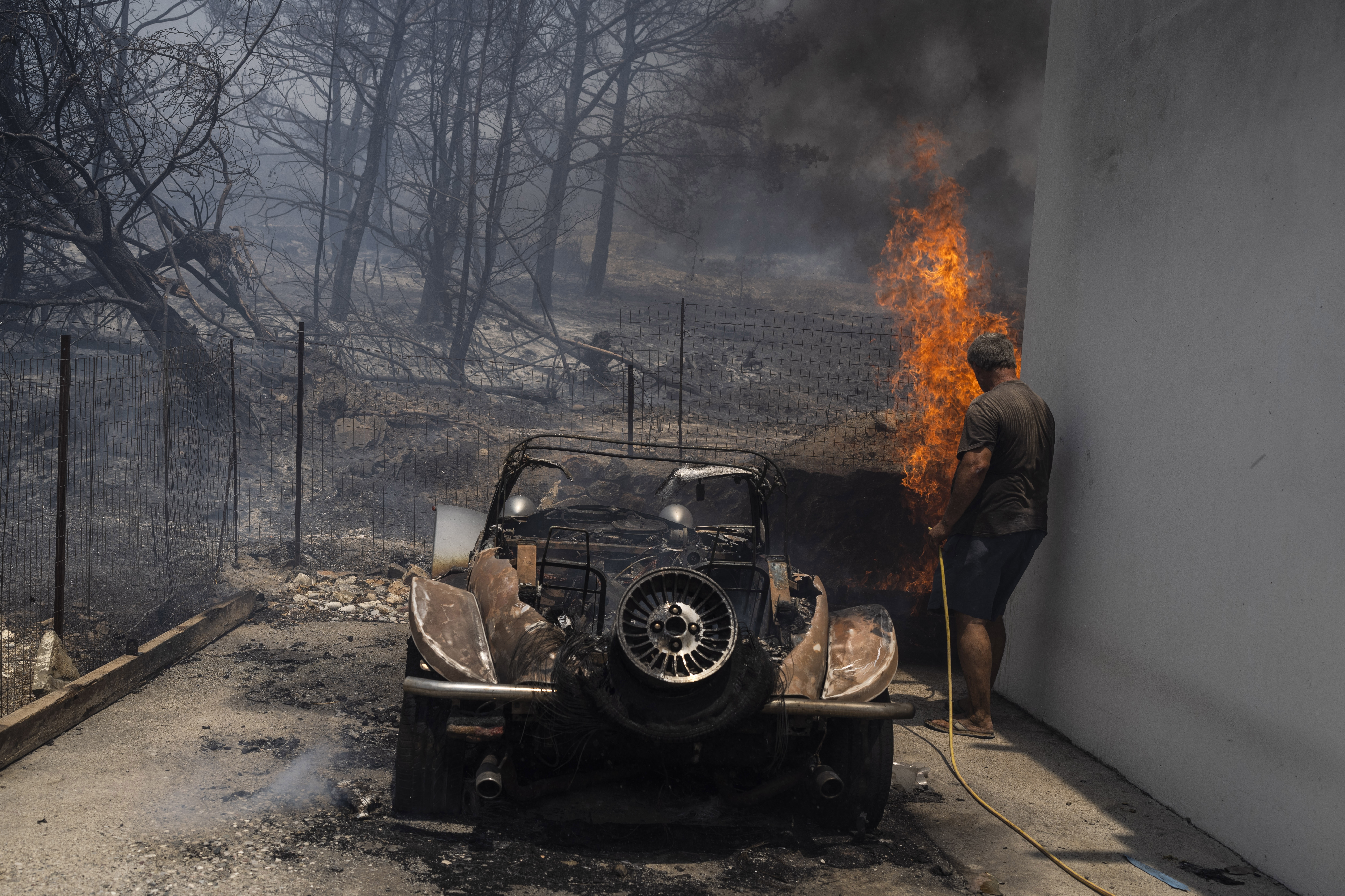 A resident tries to extinguish the flames at the yard of a house on the Aegean Sea island of Rhodes,