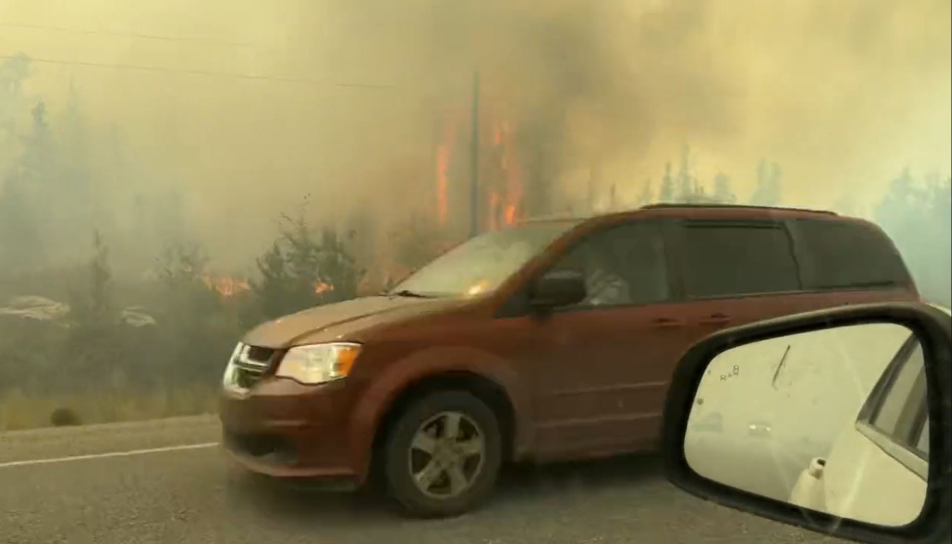 Red van driving by burning bushes on the side of the road