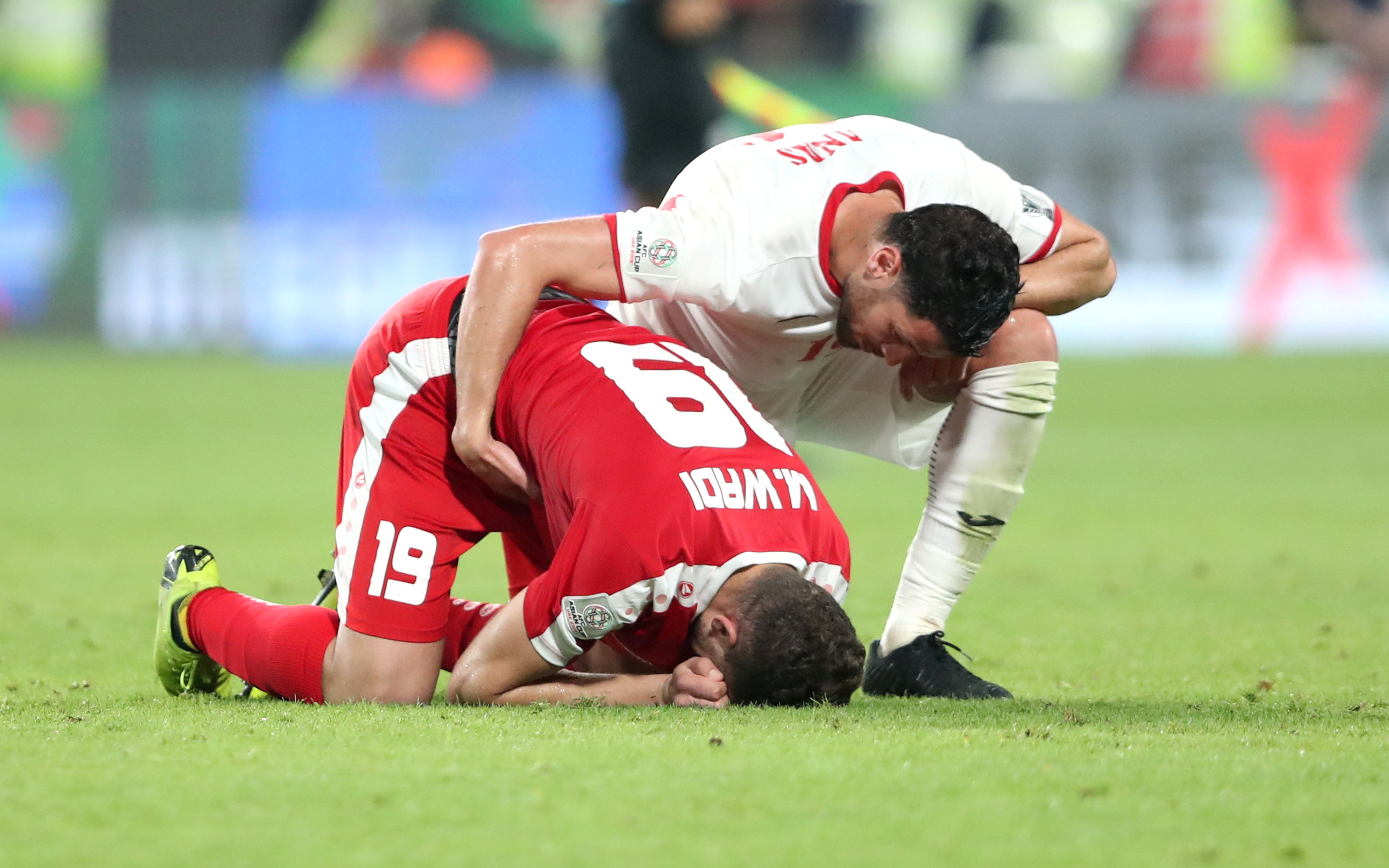 Palestine's Mahmoud Wadi sinks to the floor and folds over, while comforted by a Jordanian player