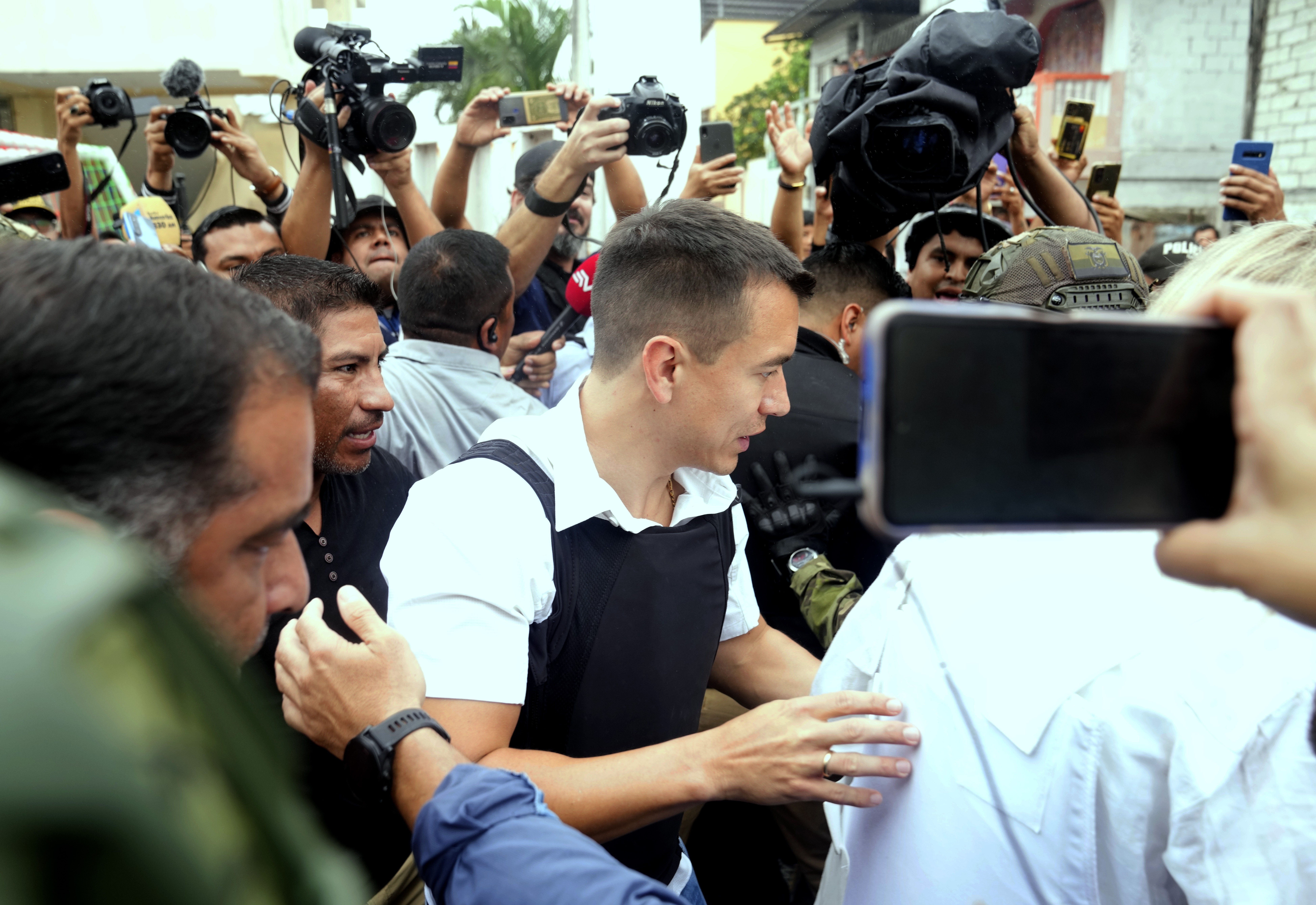 Daniel Noboa walks through a crowd wearing a flak jacket. Cameras and cellphones are pointed at him.