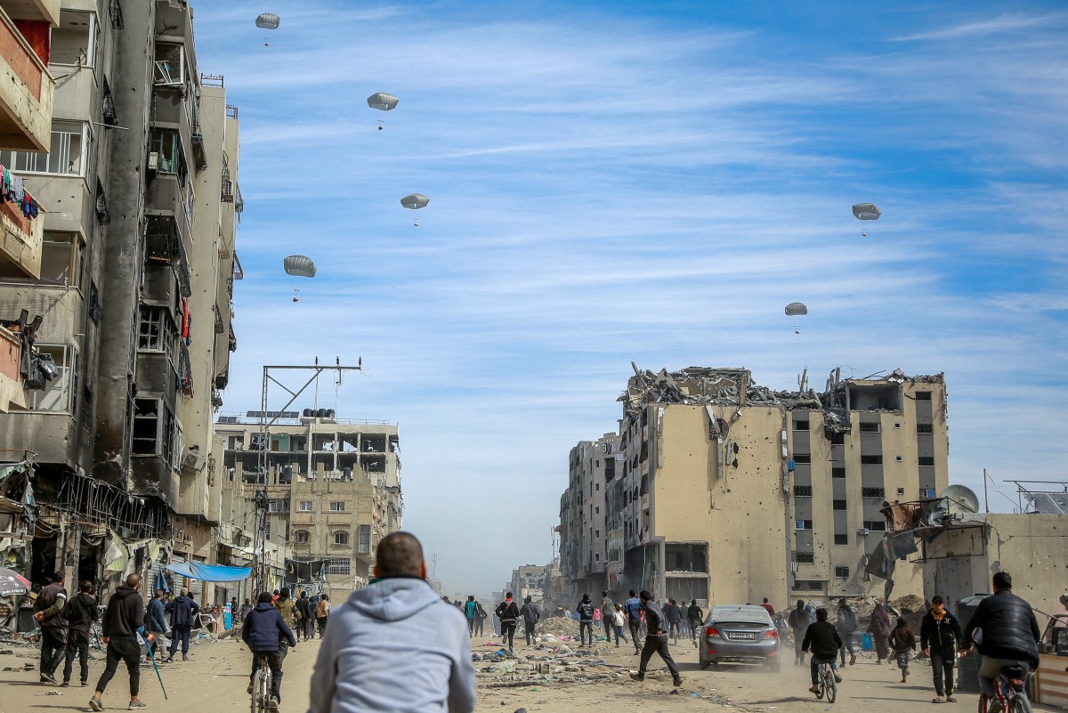 Palestinians run along a street as humanitarian aid is airdropped in Gaza City on March 1, 2024.