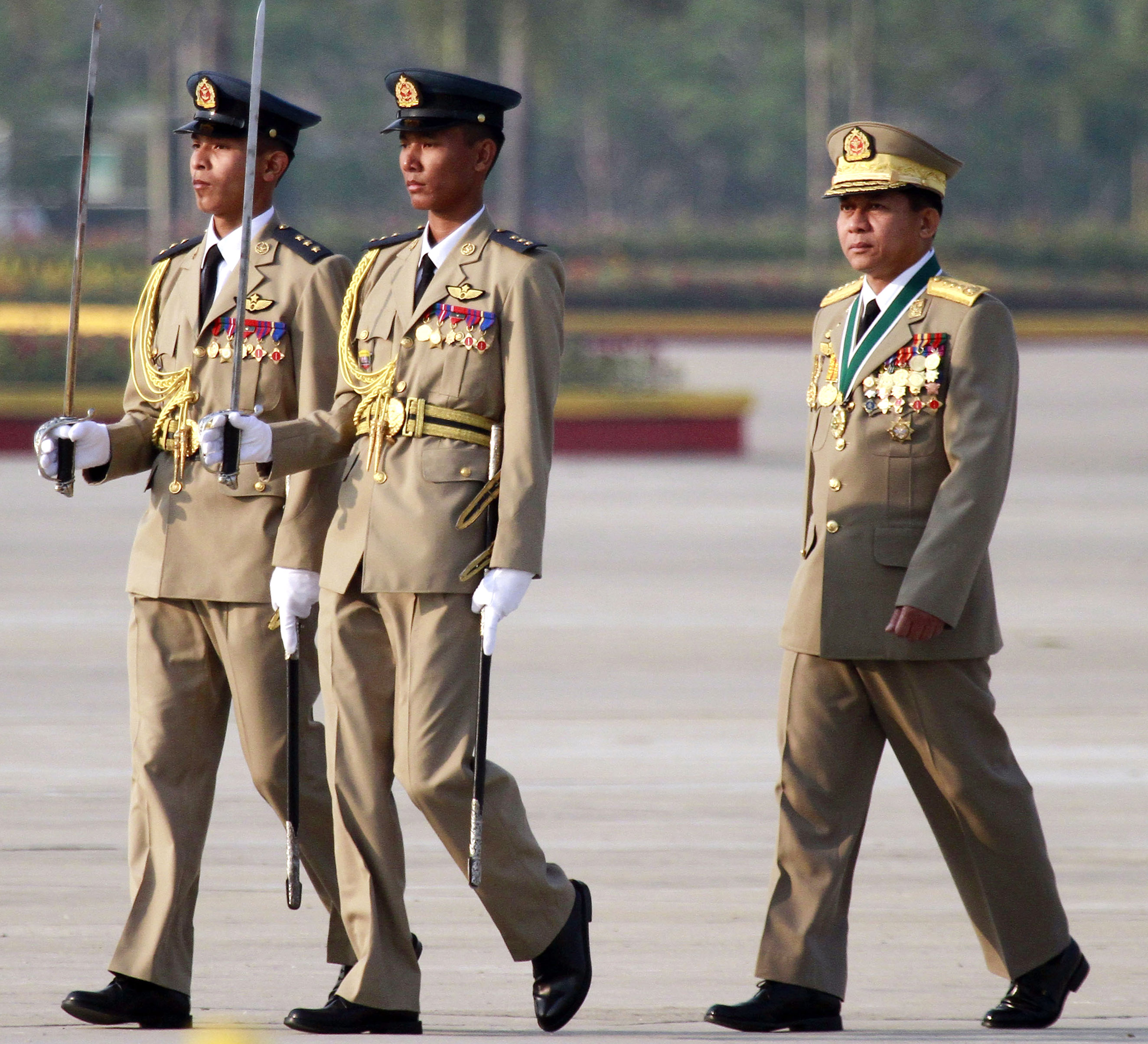 Minh Aung Hlaing at Armed Forces Day in 2012. He is accompanied by two soldiers carrying ceremonial swords. He has lots of medals on his chest.