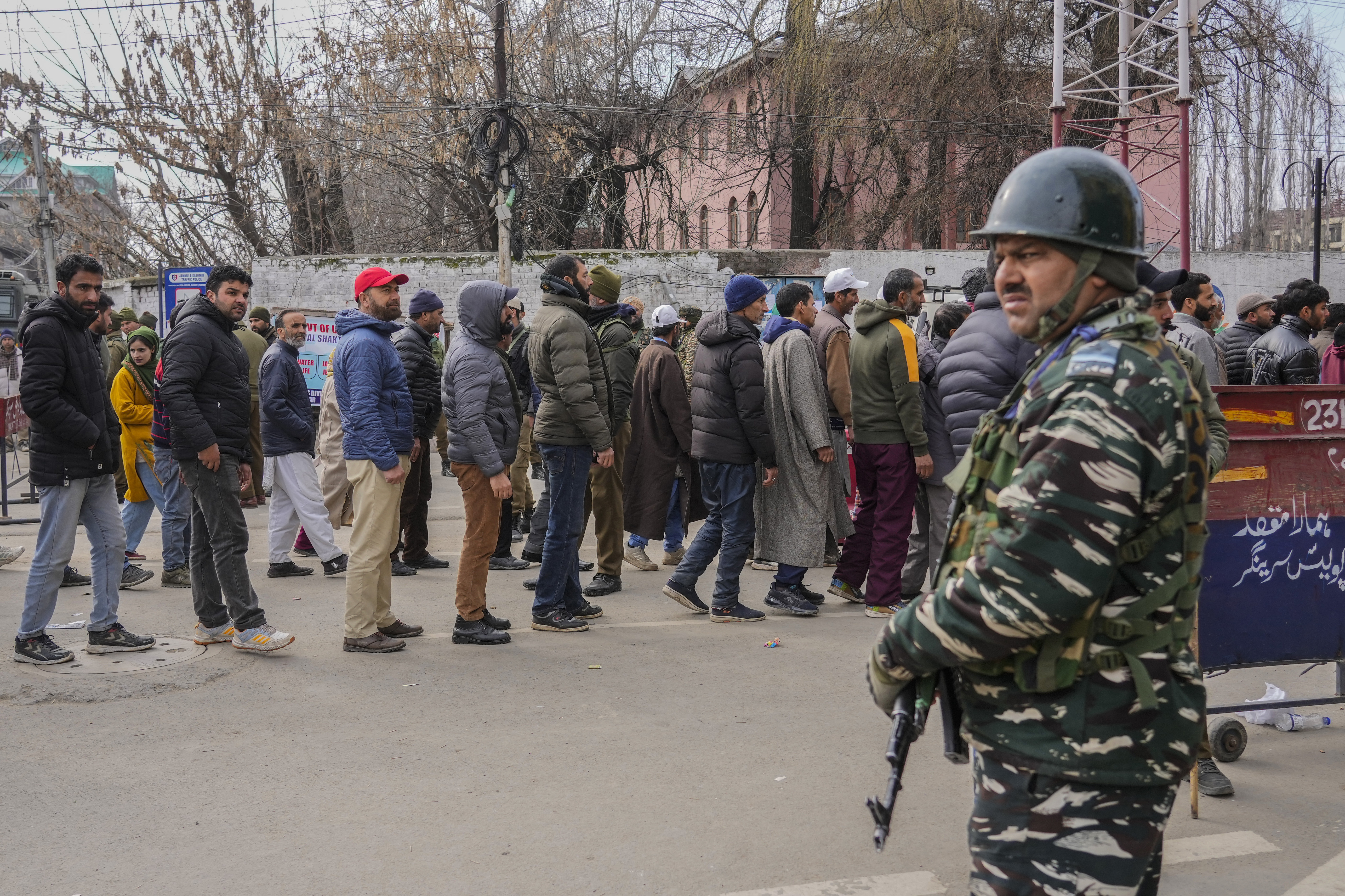 A paramilitary soldier stands guard as people queue up for a security check outside the stadium in Srinagar where PM Narendra Modi held the rally