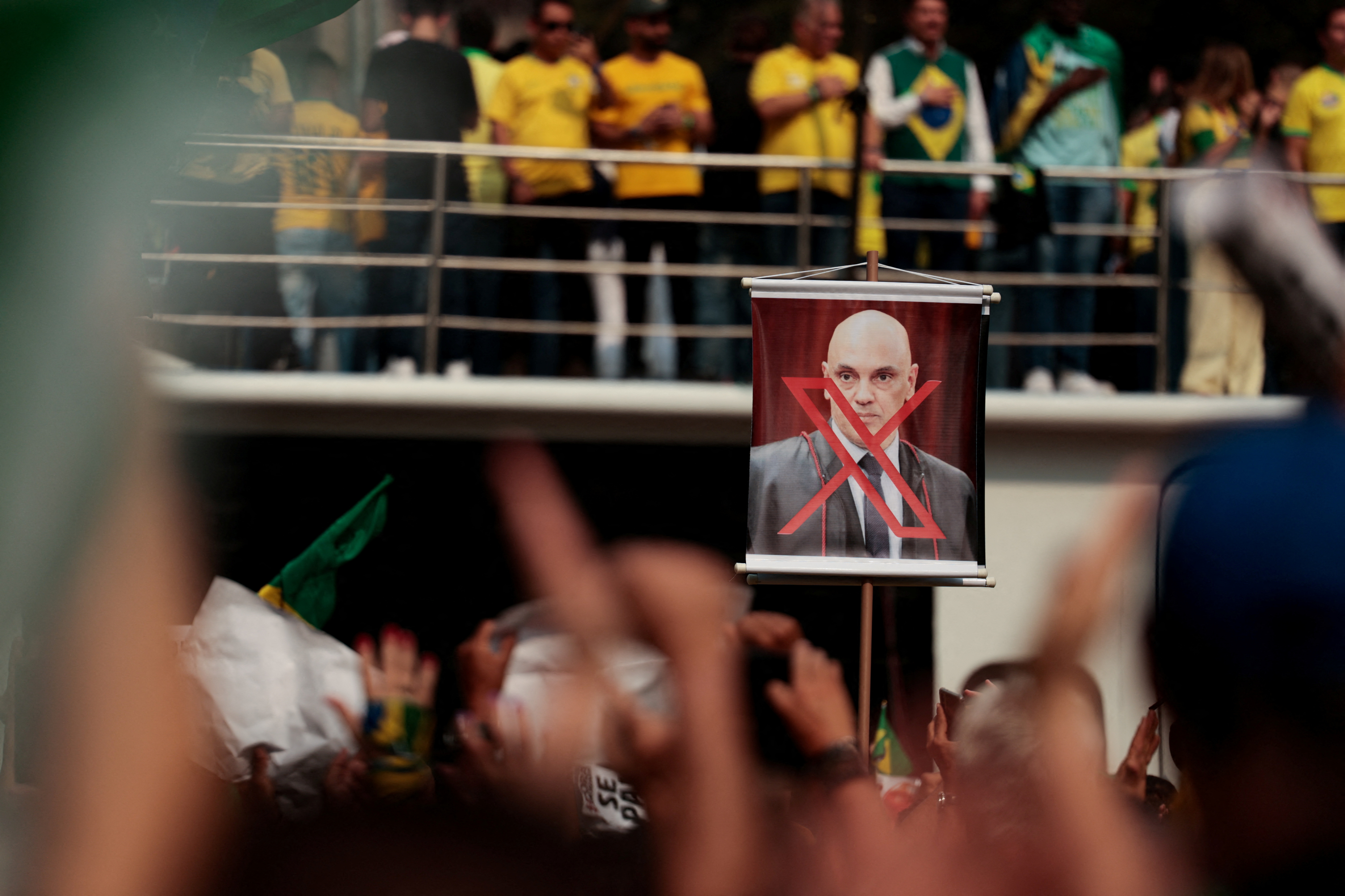 A protester holds up a sign with a photo of Alexandre de Moraes crossed out by Twitter's X logo.