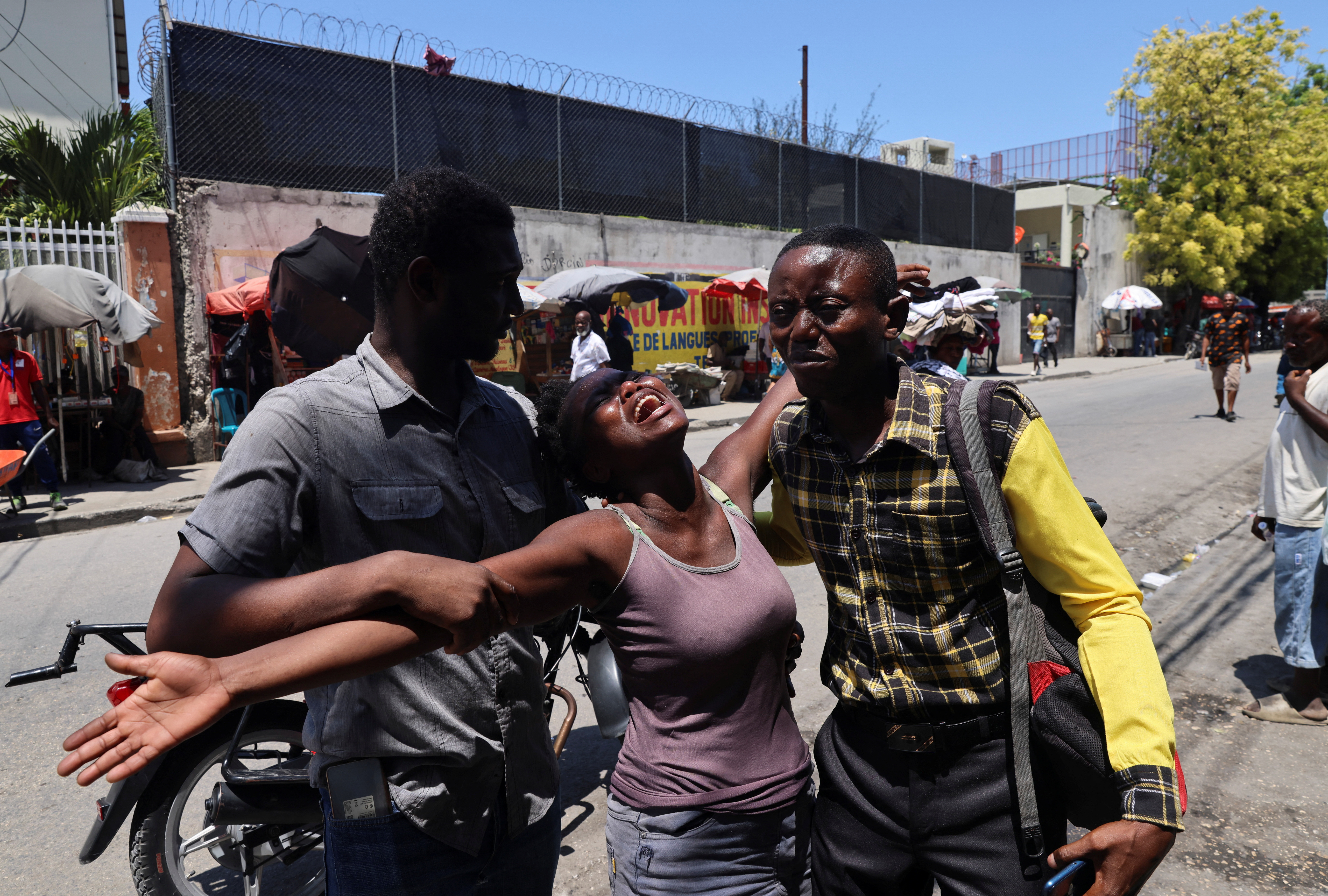 A Haitian woman is helped by others as she reacts upon seeing the dead body of her brother