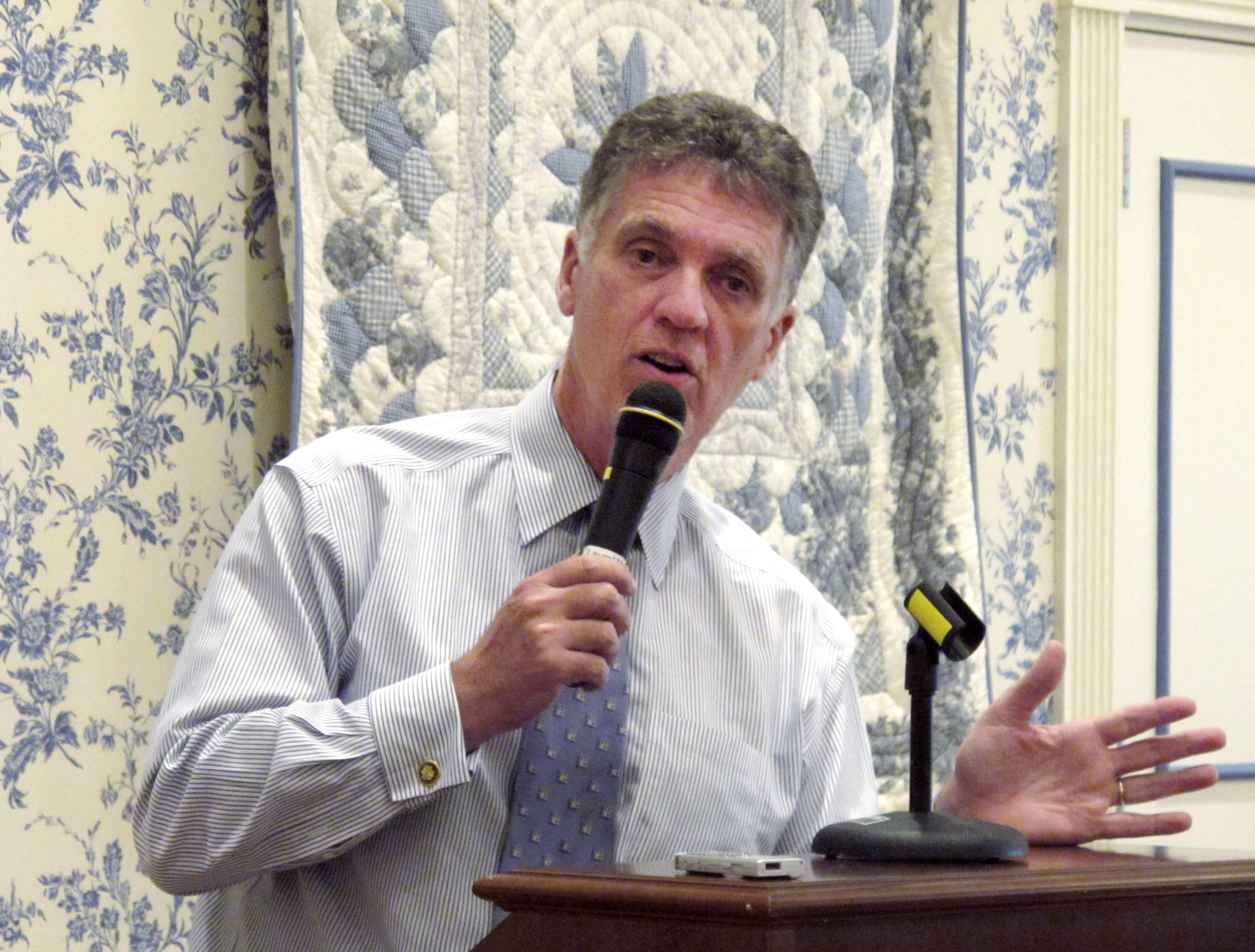 Dave Weldon speaks into a handheld microphone behind a podium.