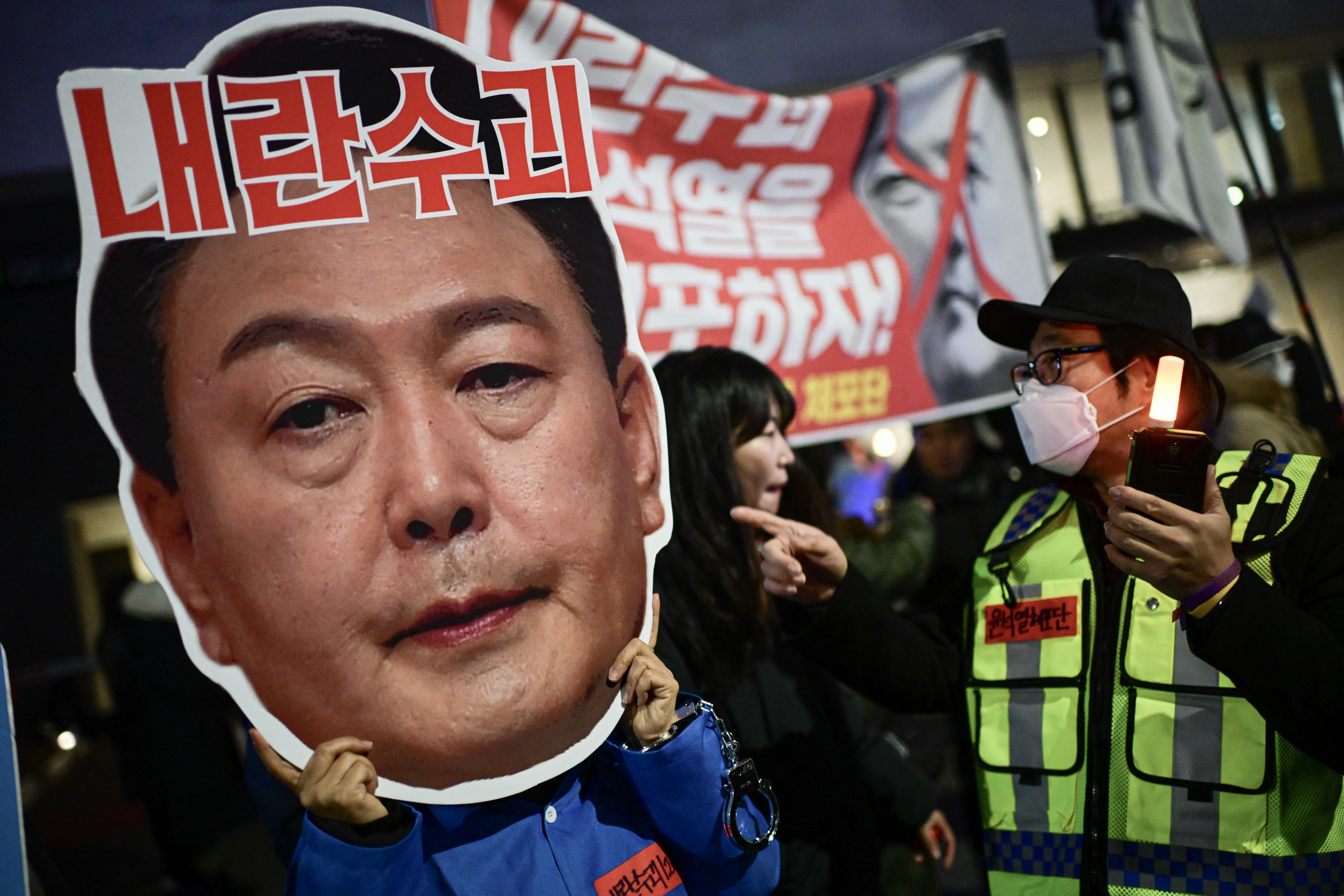 A protester holding a cardboard reading ‘Leader of insurgents’ on an image depicting the face of President Yoon Suk-yeol takes part in a protest calling for his ouster outside the National Assembly in Seoul, December 8, 2024