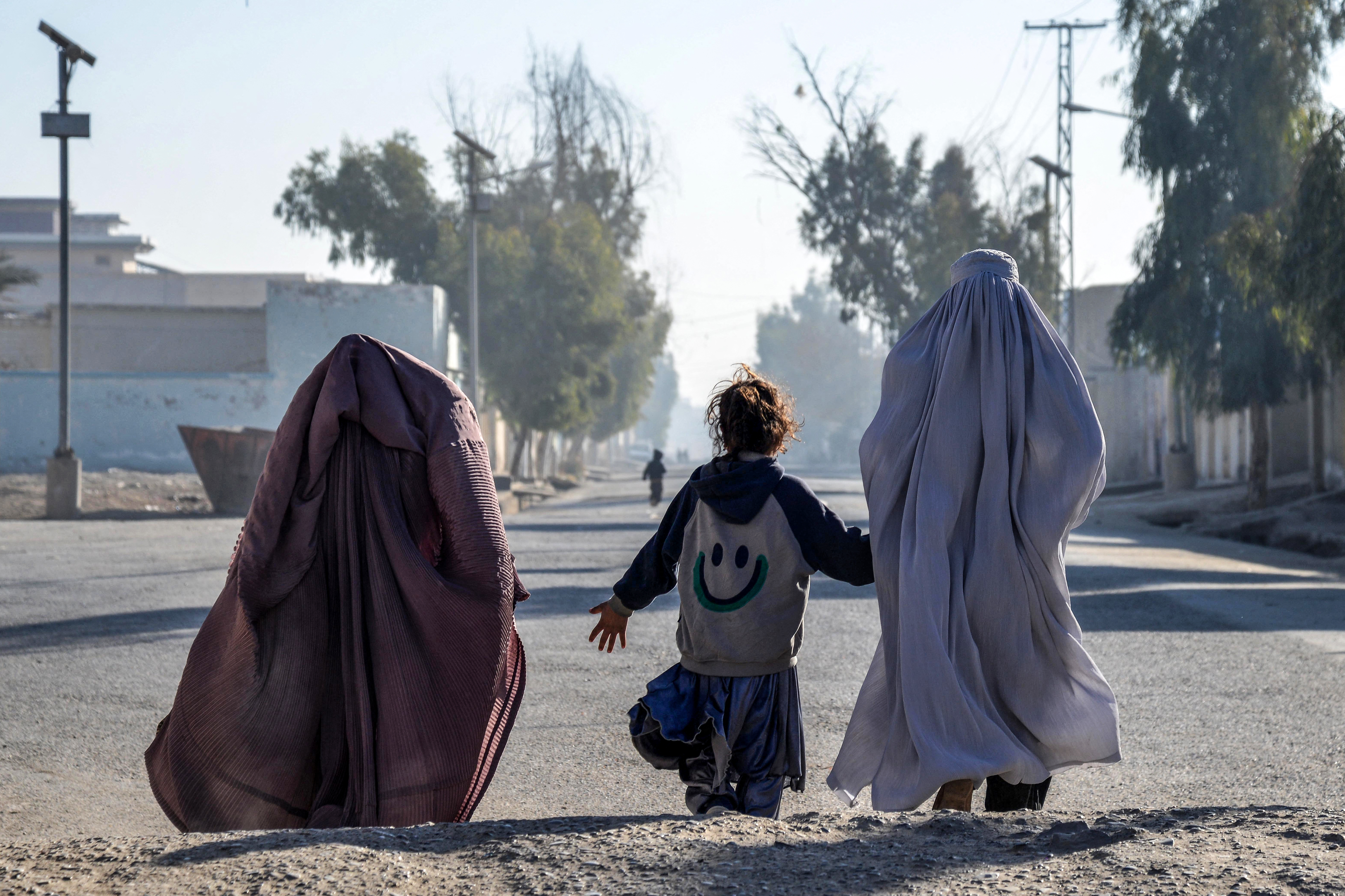 Afghan burqa-clad women and a girl walk along a street in Kandahar on December 29, 2024. (Photo by Sanaullah SEIAM / AFP)
