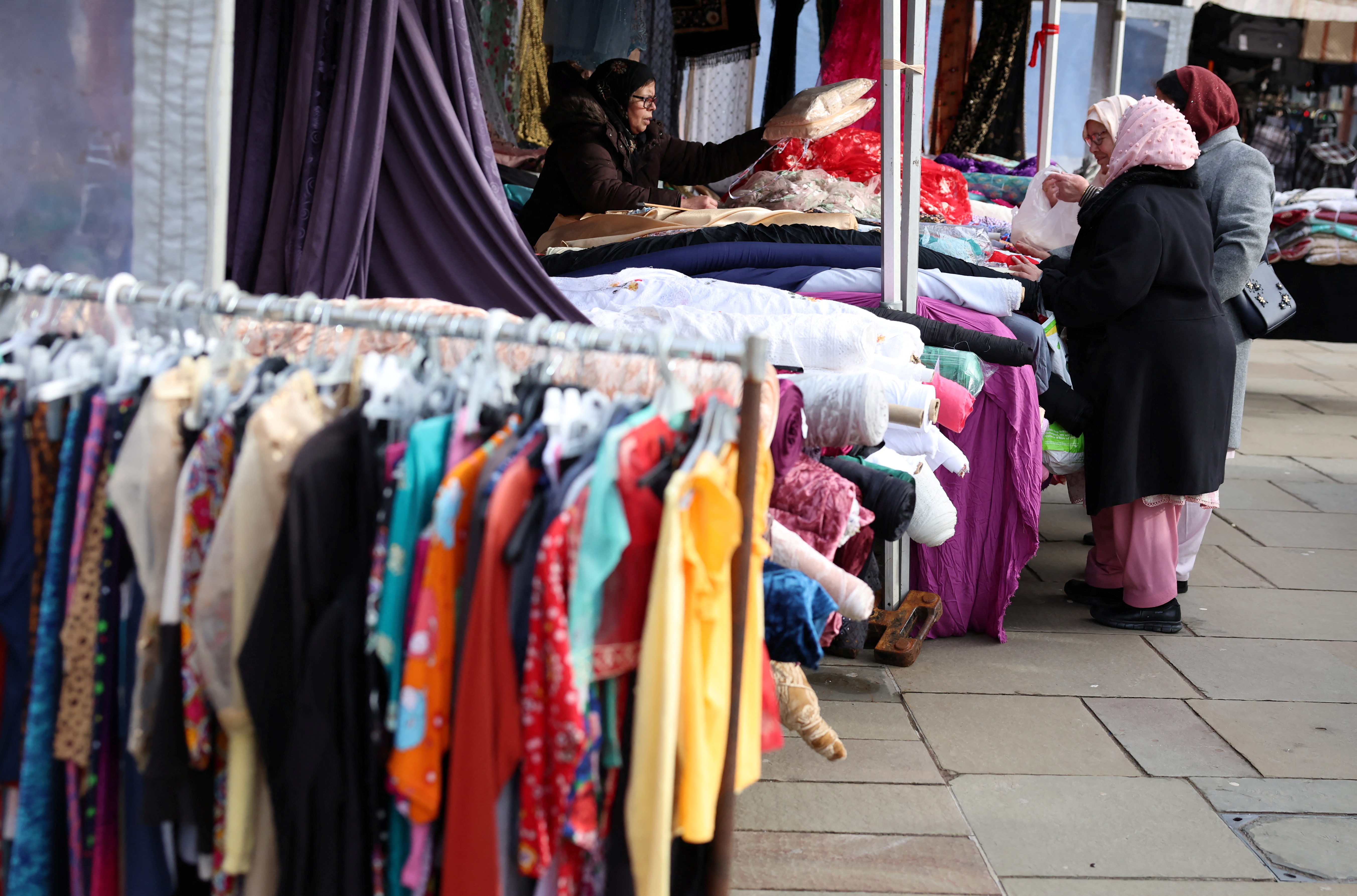 Women buy material from a market stall.