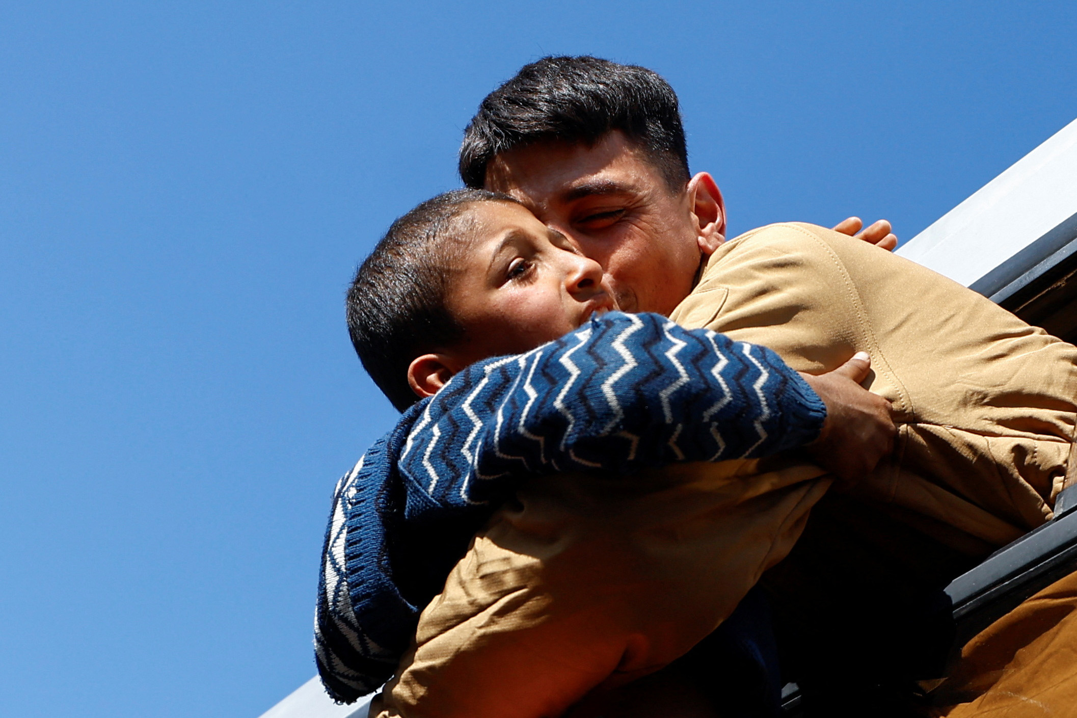 a young man embraces a child against a blue sky